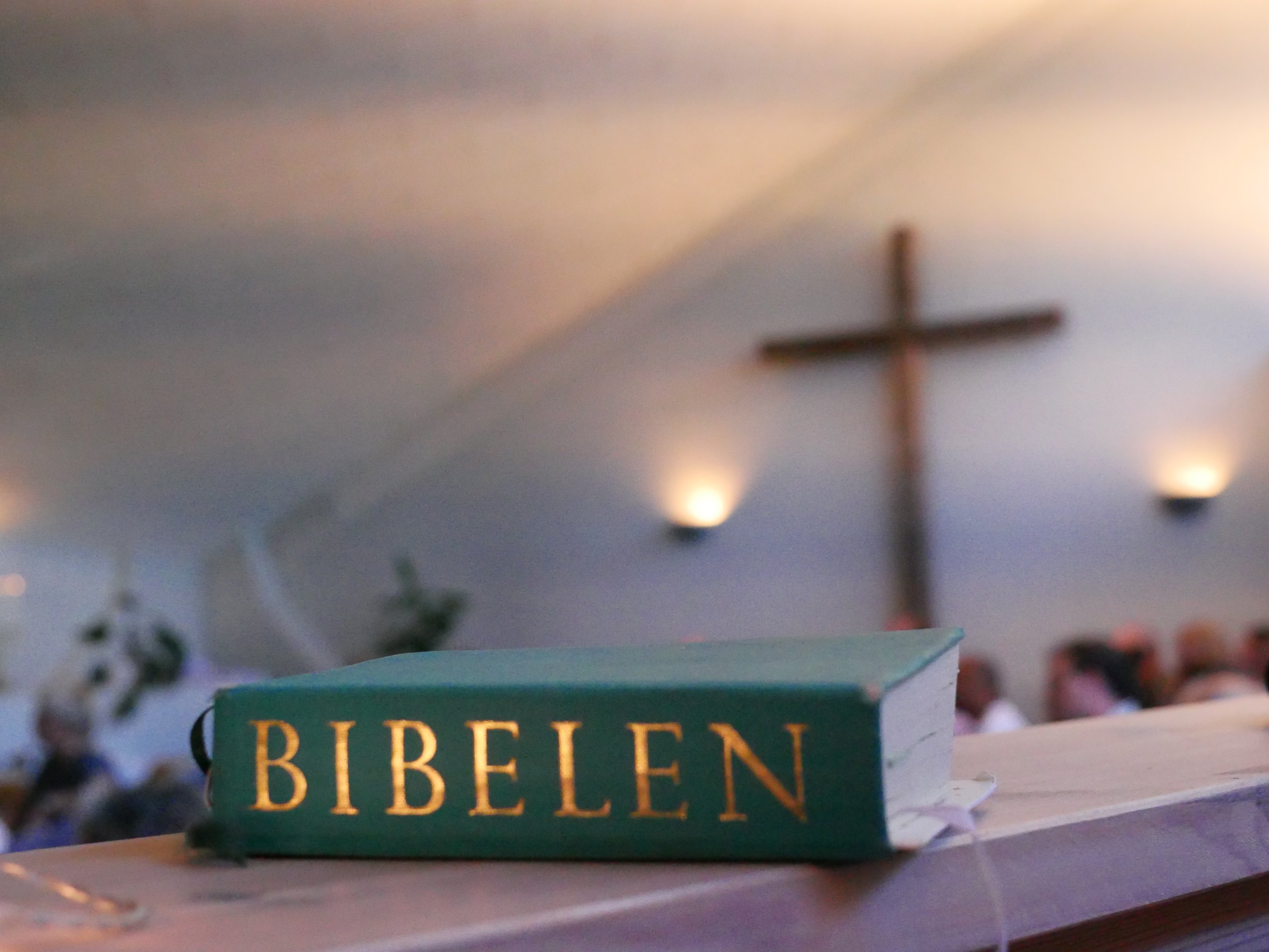 En bibel liggende på en hylde i en Pinsekirken Svendborg med kors i baggrunden.
