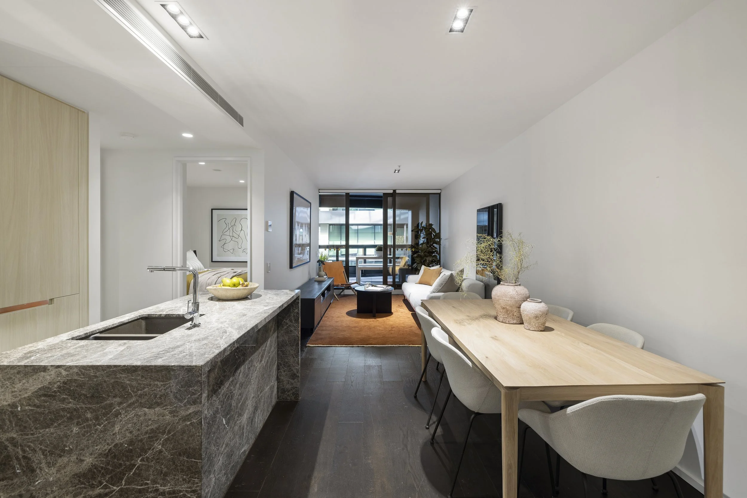 Open-concept living room and dining area with kitchen island, modern furniture, and balcony in a contemporary apartment.