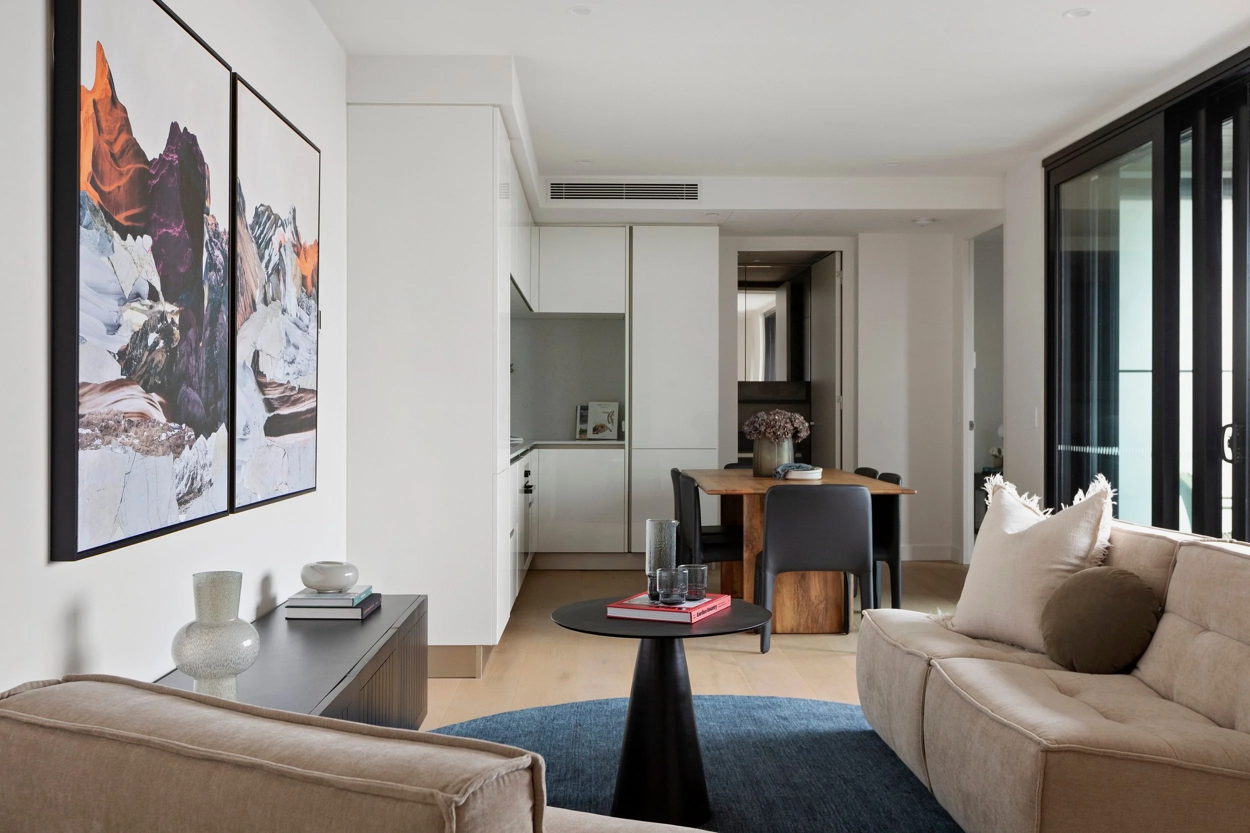 Modern living room with beige sofa, black coffee table, wall art, and large sliding glass doors leading outside.