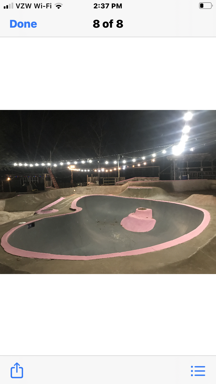 Empty outdoor skatepark at night with pink accents and string lights overhead.