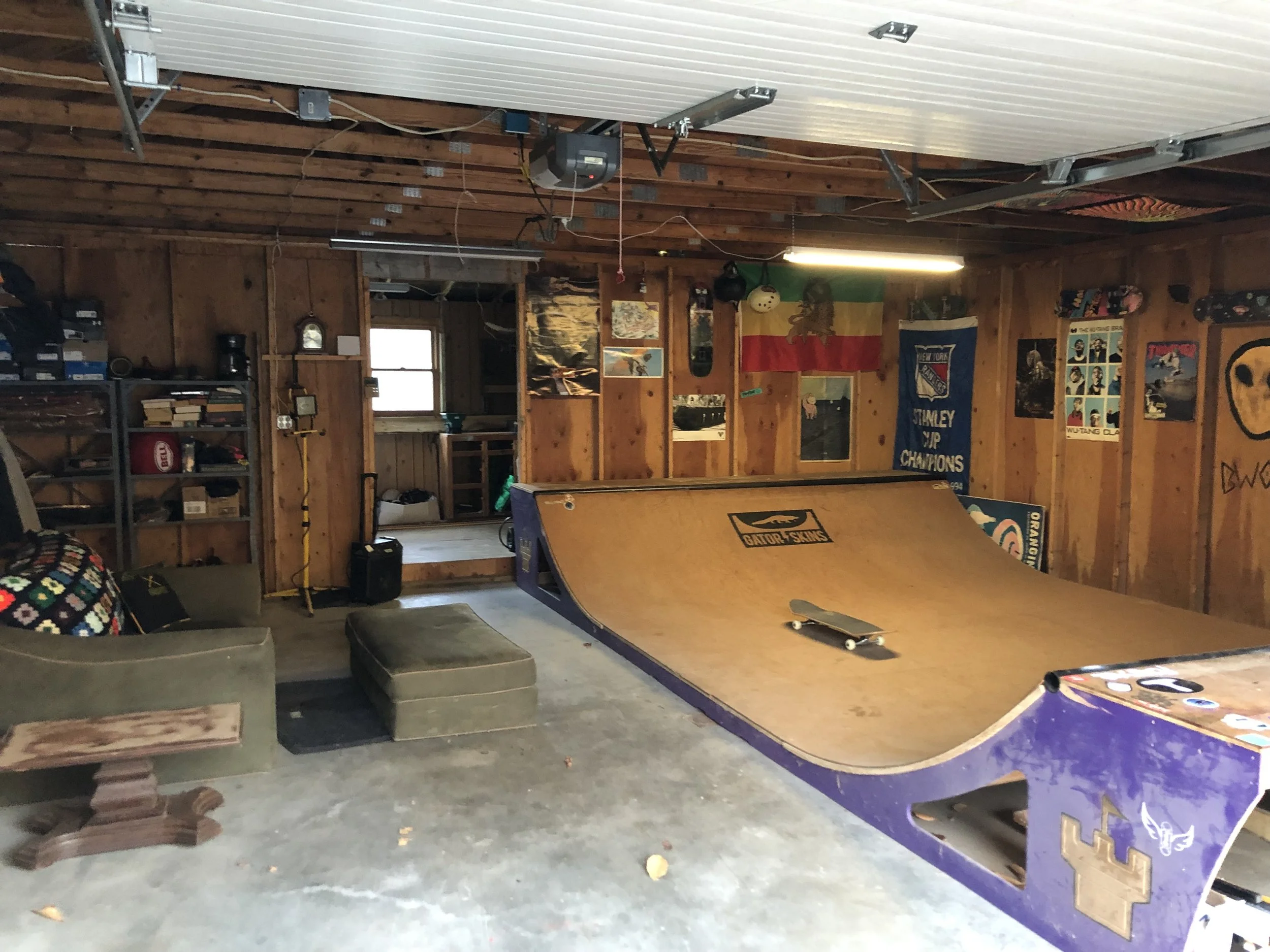 Indoor skateboarding ramp in a garage with posters and flags on the wood-paneled walls.