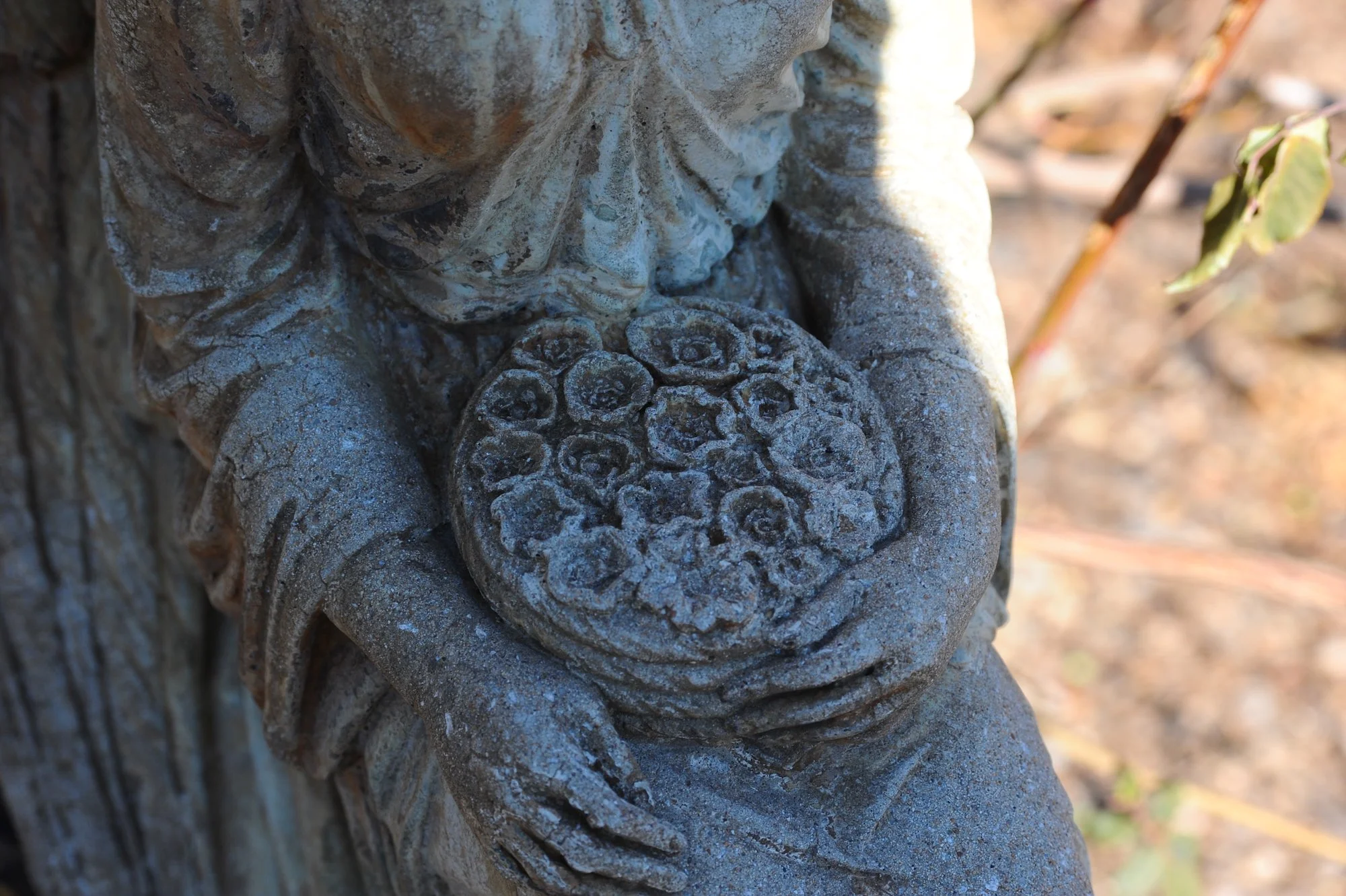 Close-up of a weathered stone sculpture of a person holding a flower-like object