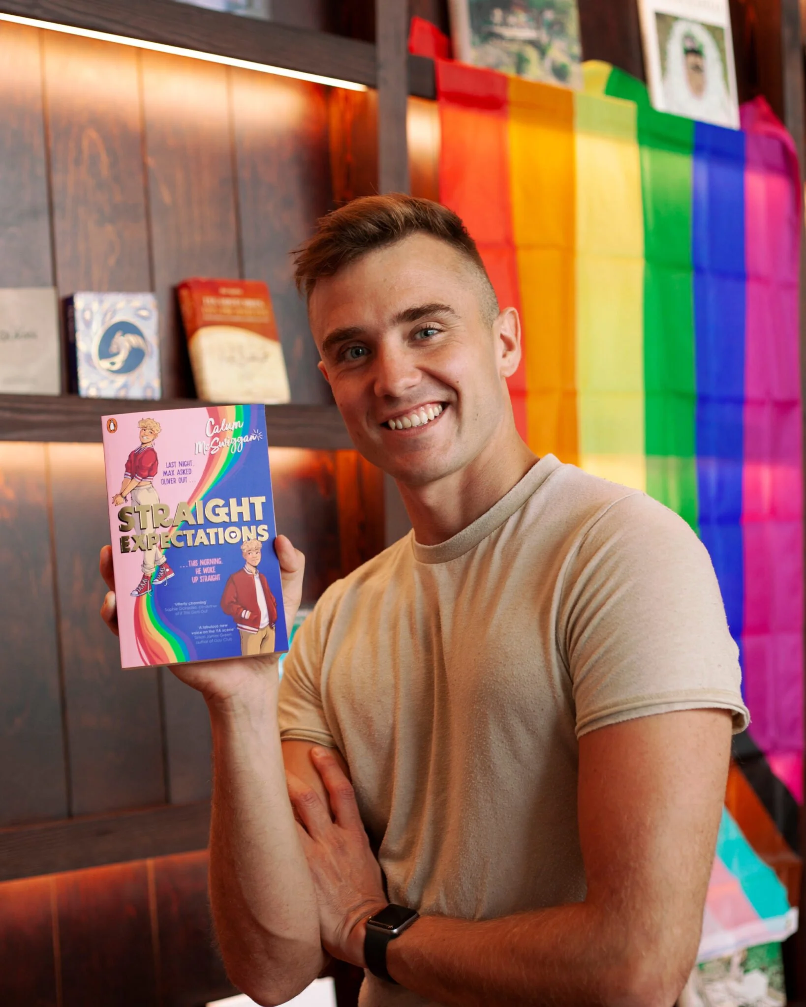 a man holds a book that says "straight expectations" in front of a pride flag