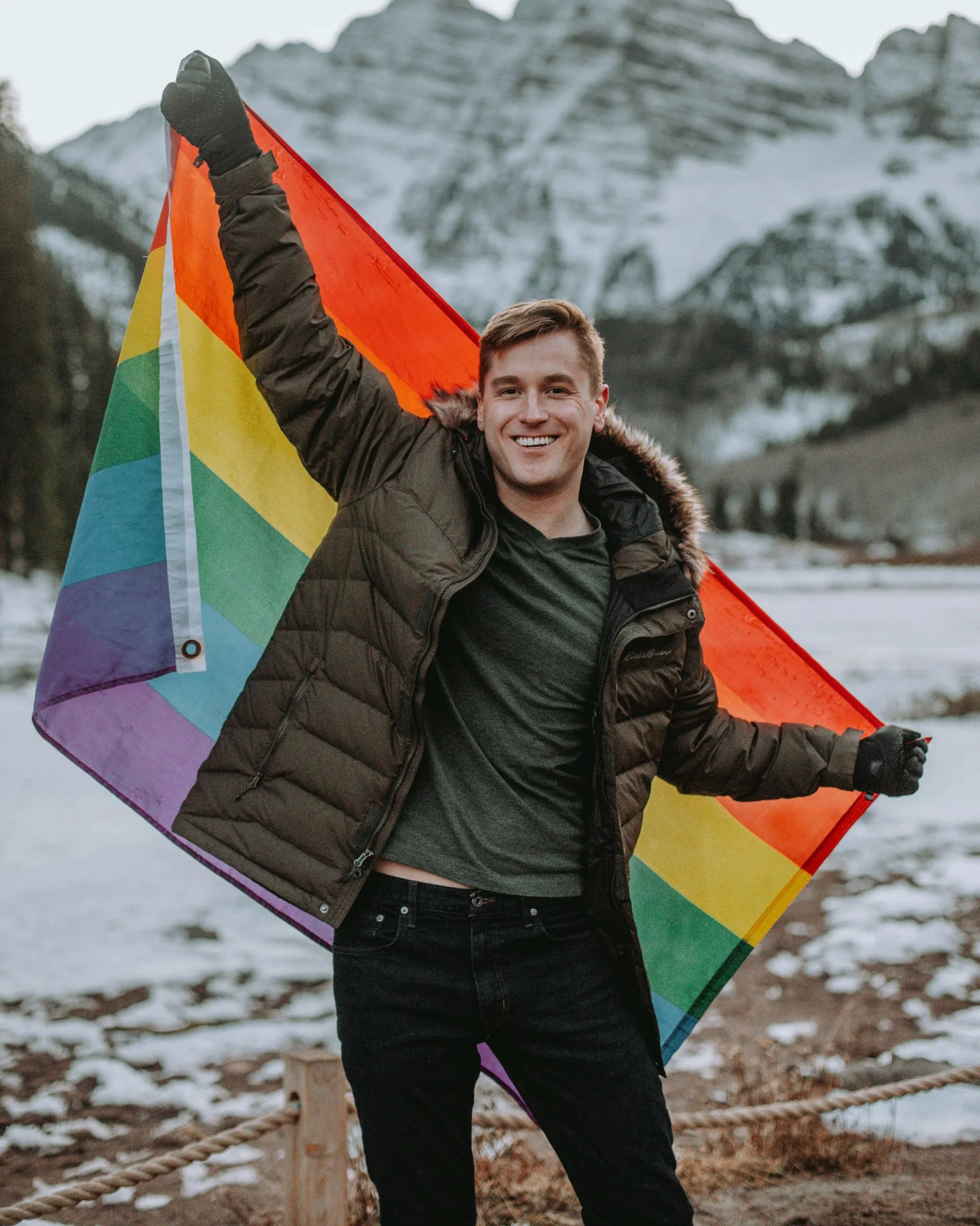 Man holds a rainbow pride flag in front of a snowy mountain