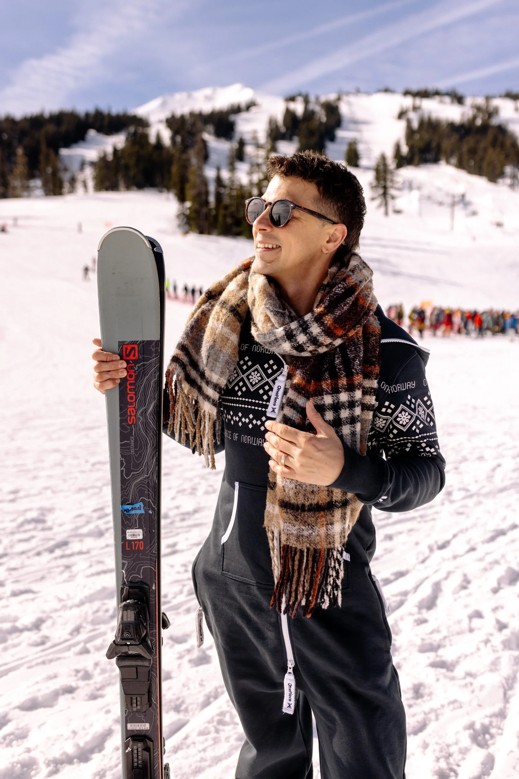 Smiling skier holding Salomon skis on a sunny snow-covered slope in Bend, Oregon.