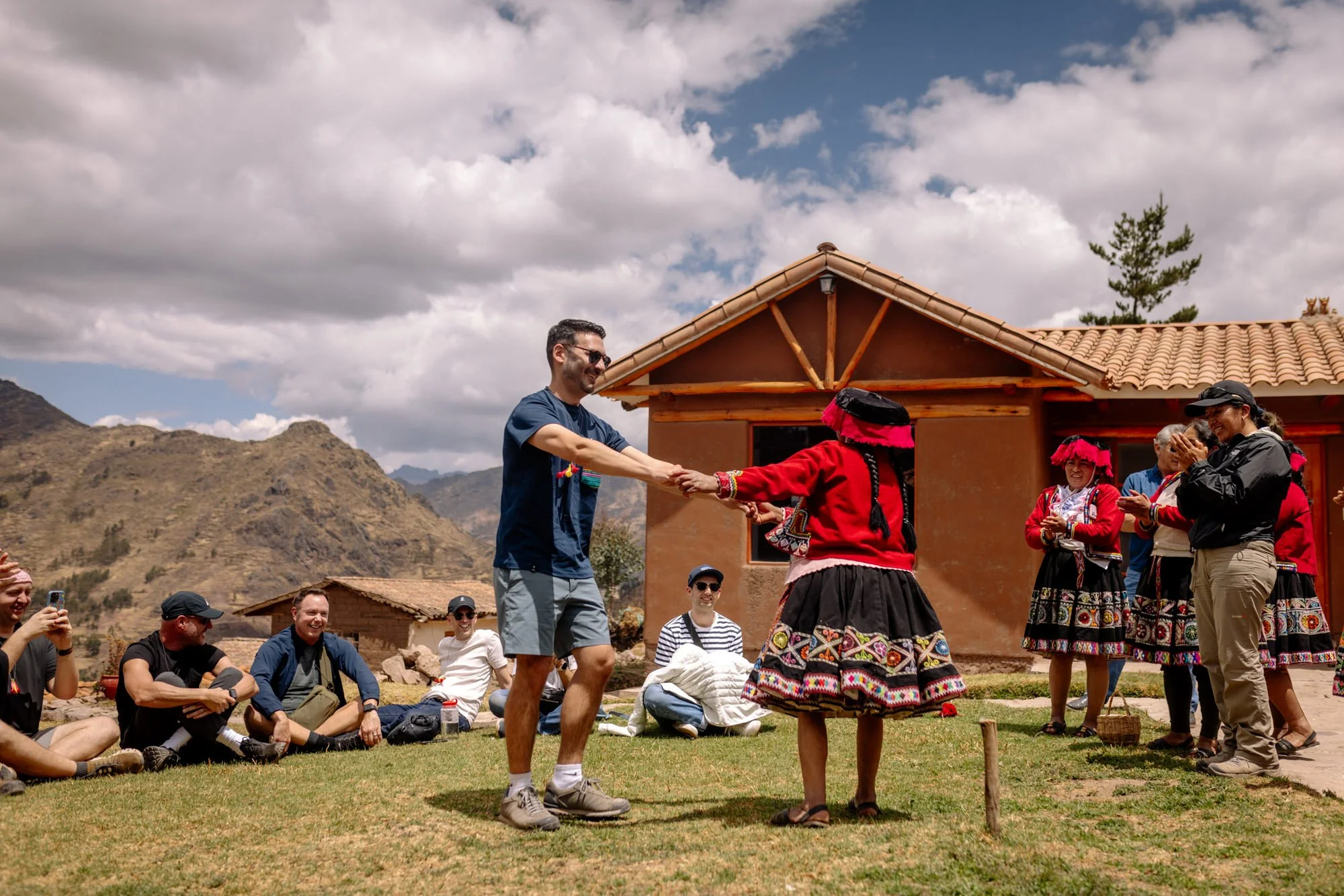 Tourist dancing with a local woman in traditional dress in Peru's Sacred Valley, crowd cheering.