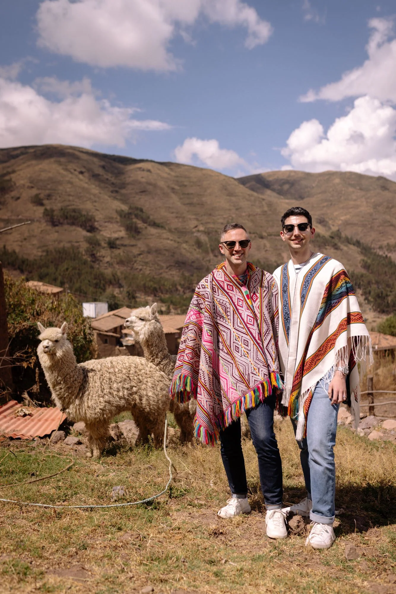 Two men in traditional Andean ponchos posing with an alpaca in the Sacred Valley, Peru.