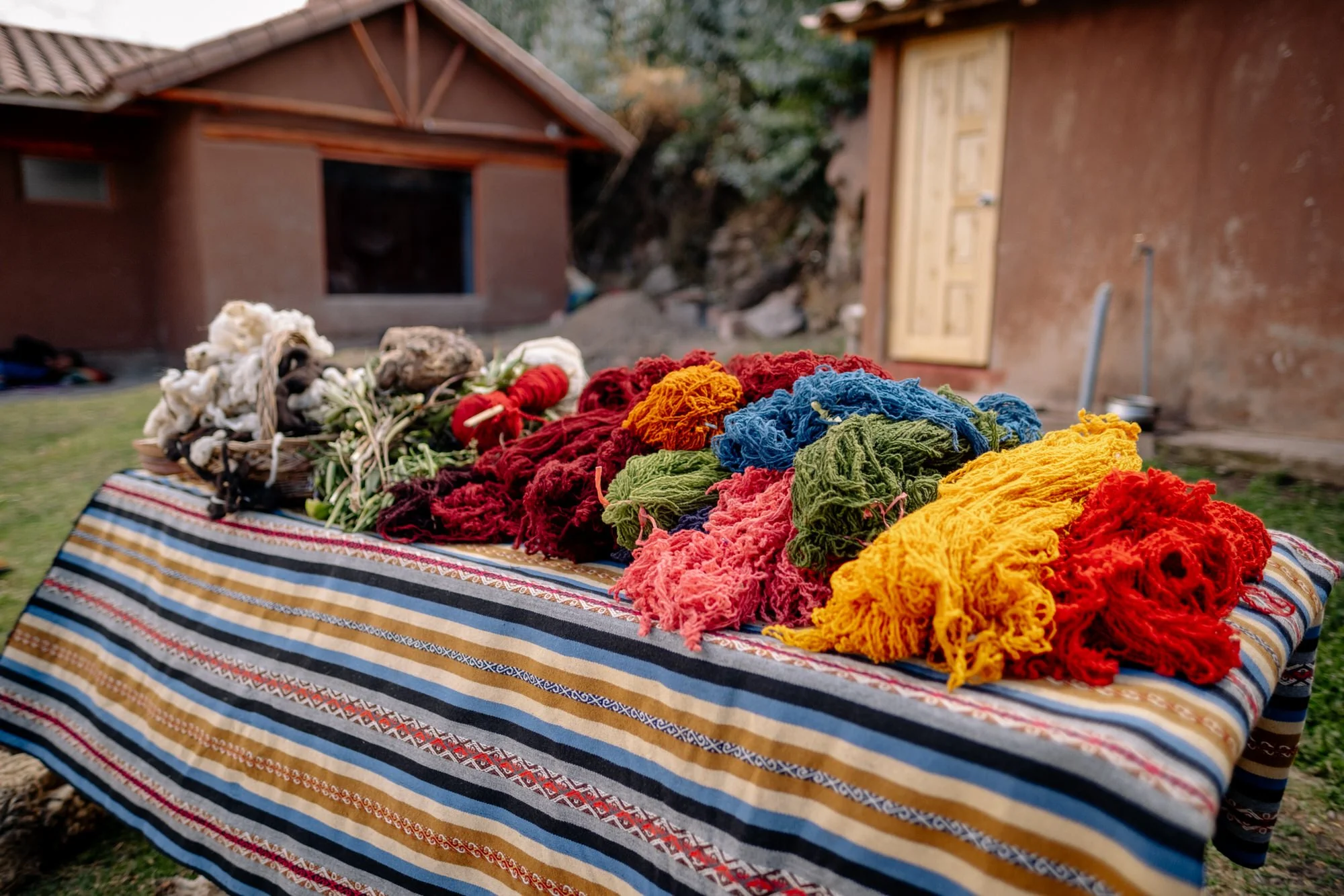 Vibrant skeins of naturally dyed alpaca wool displayed on a woven textile table in Peru's Sacred Valley.