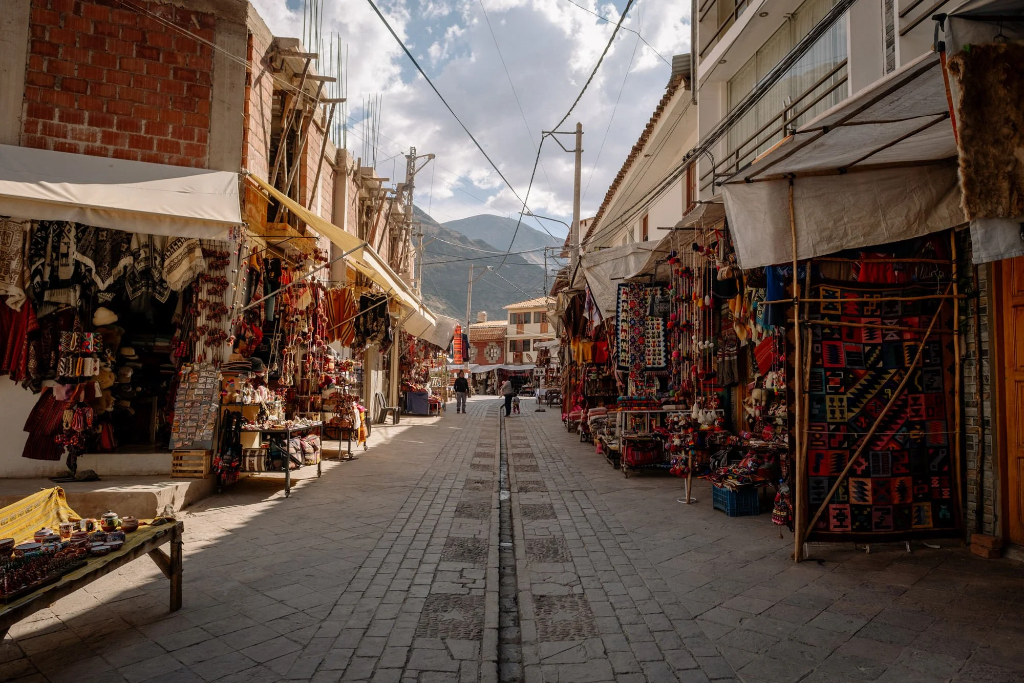 Shoppers browse colorful handicraft stalls lining a narrow cobblestone alley in Pisac, Peru.