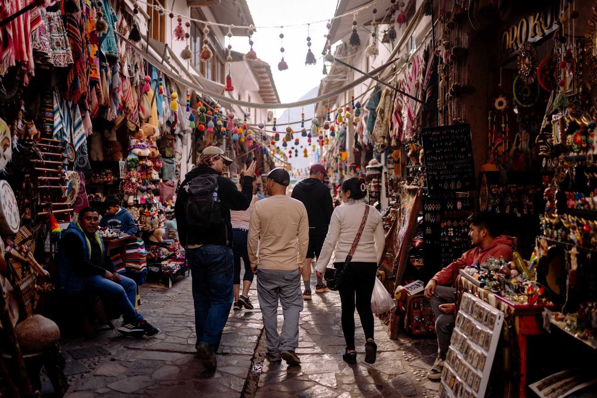 Shoppers browse colorful handicraft stalls lining a narrow cobblestone alley in Pisac, Peru.