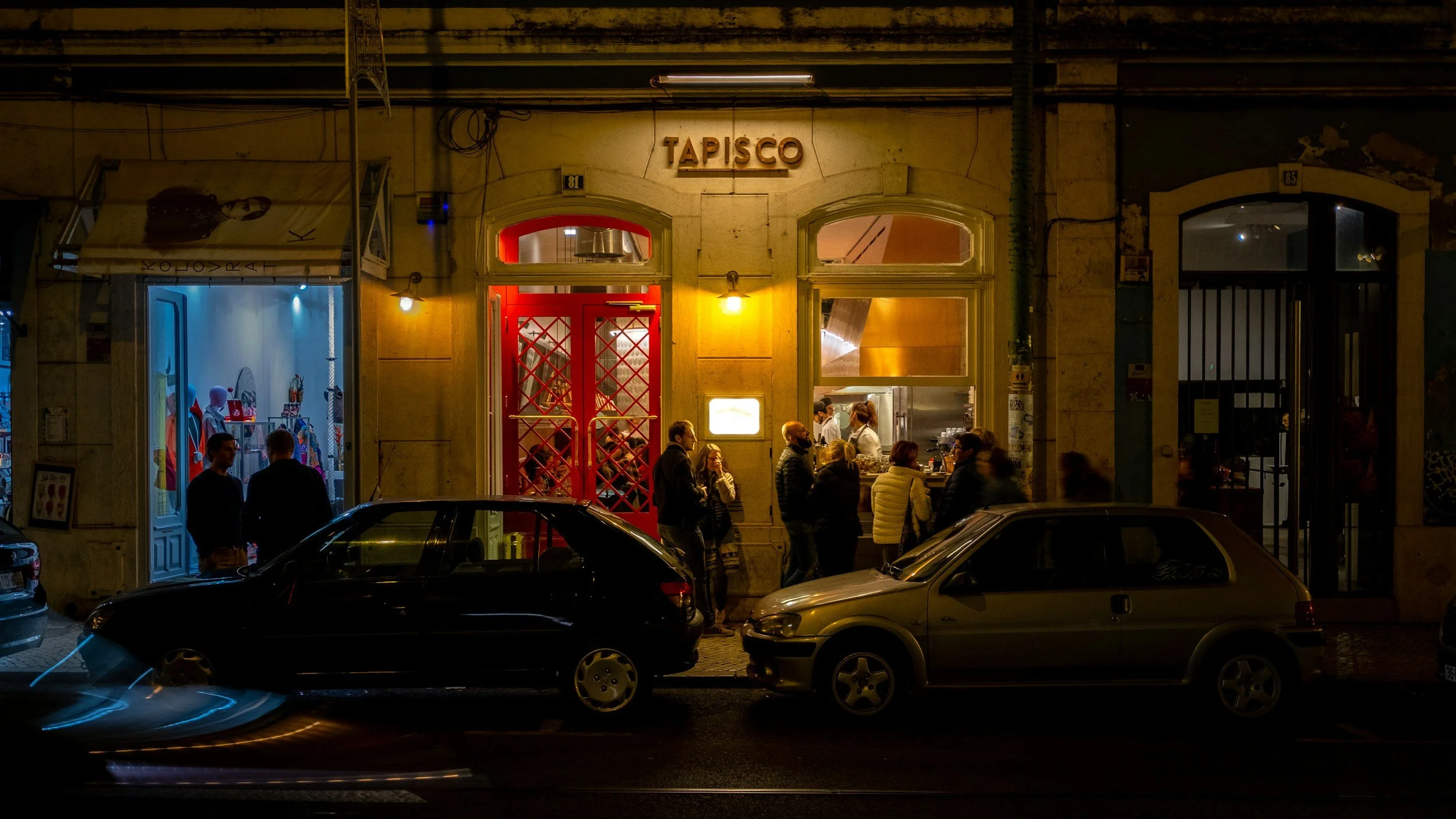 people gather at night outside a restaurant with a sign that says Tapisco.