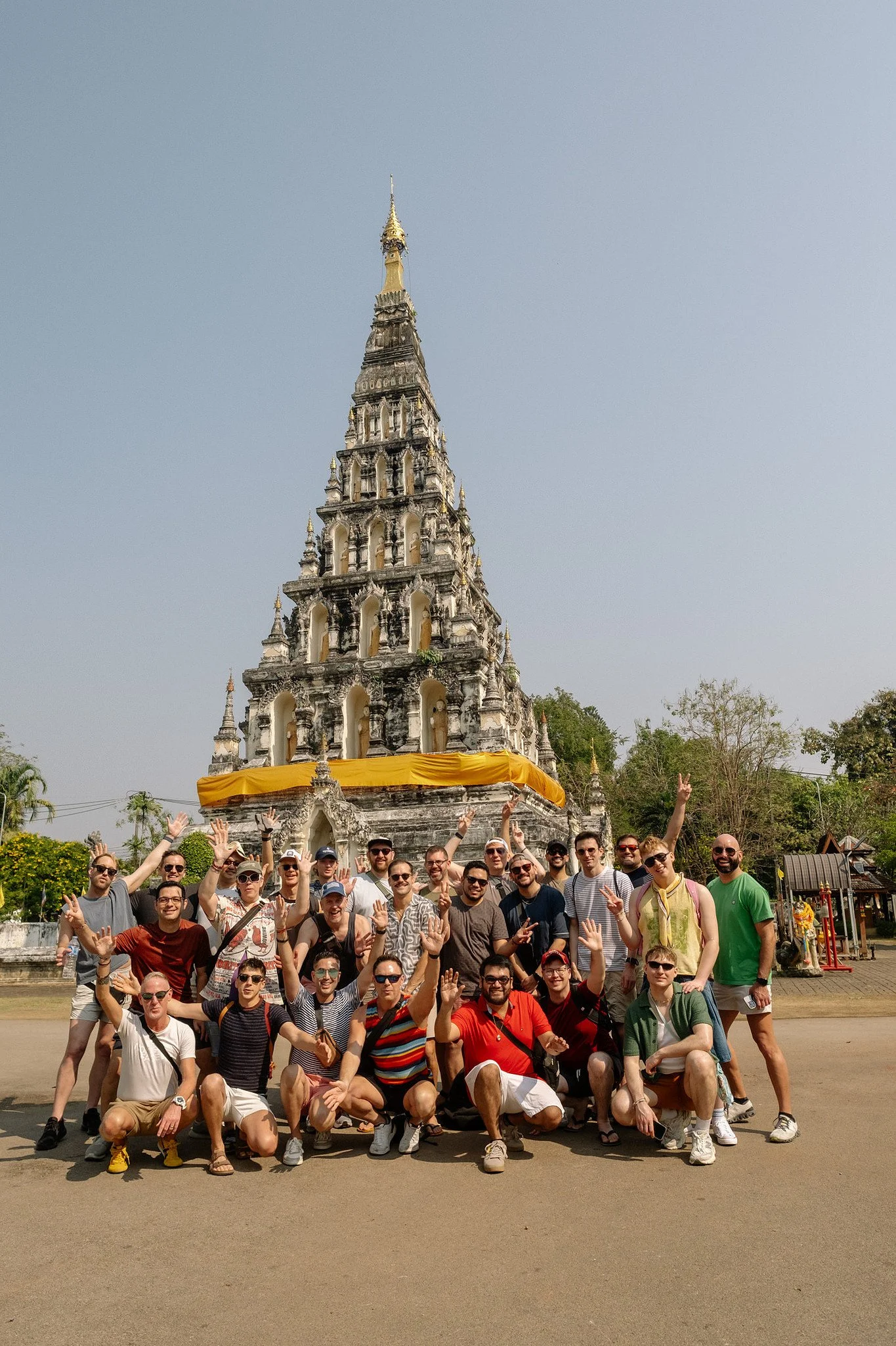 Group cheering with raised hands in front of the ancient chedi at Wat Chedi Luang, Chiang Mai, Thailand