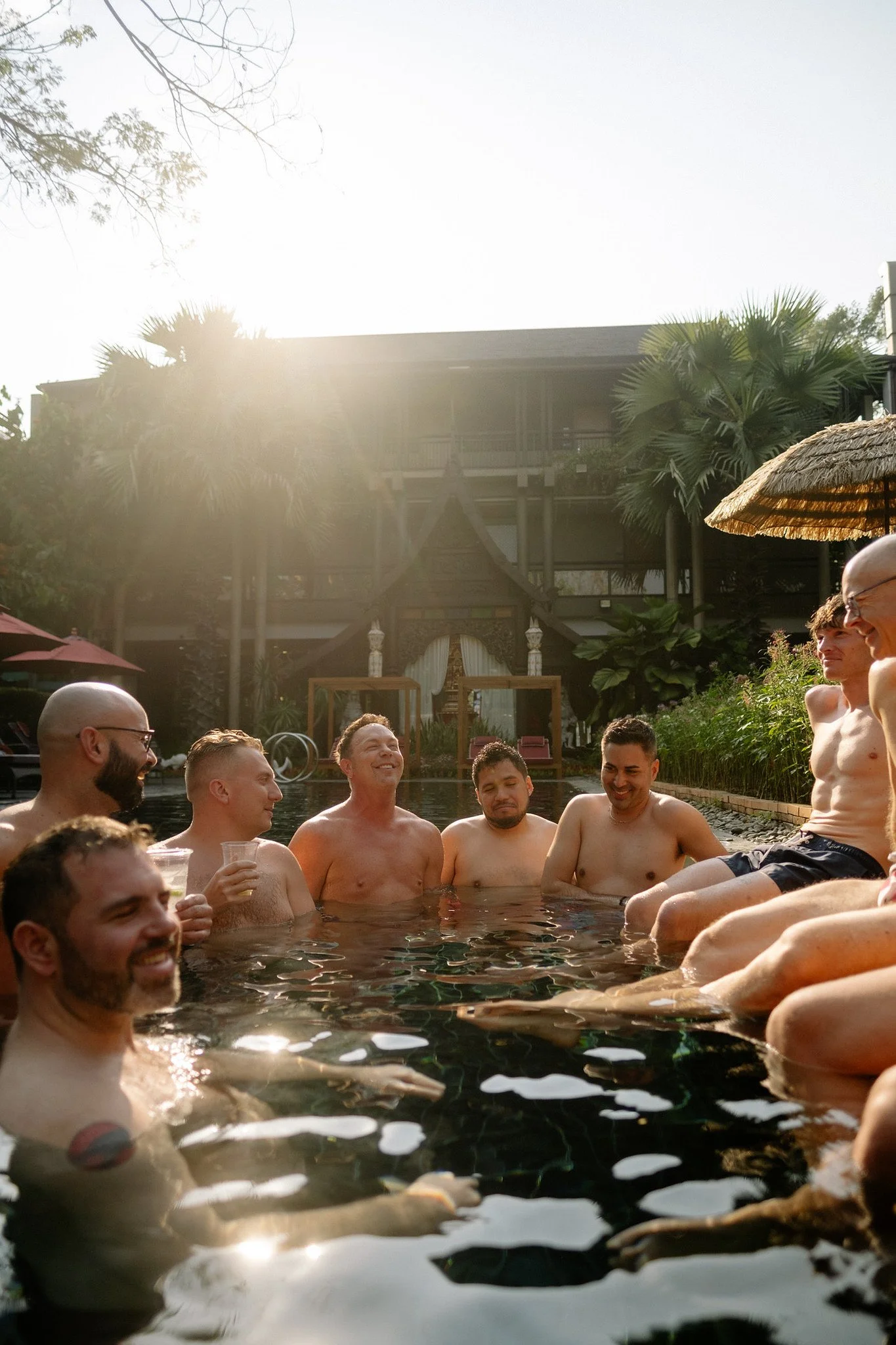 SideQuests travelers relaxing and laughing together in a resort swimming pool at golden hour in Thailand