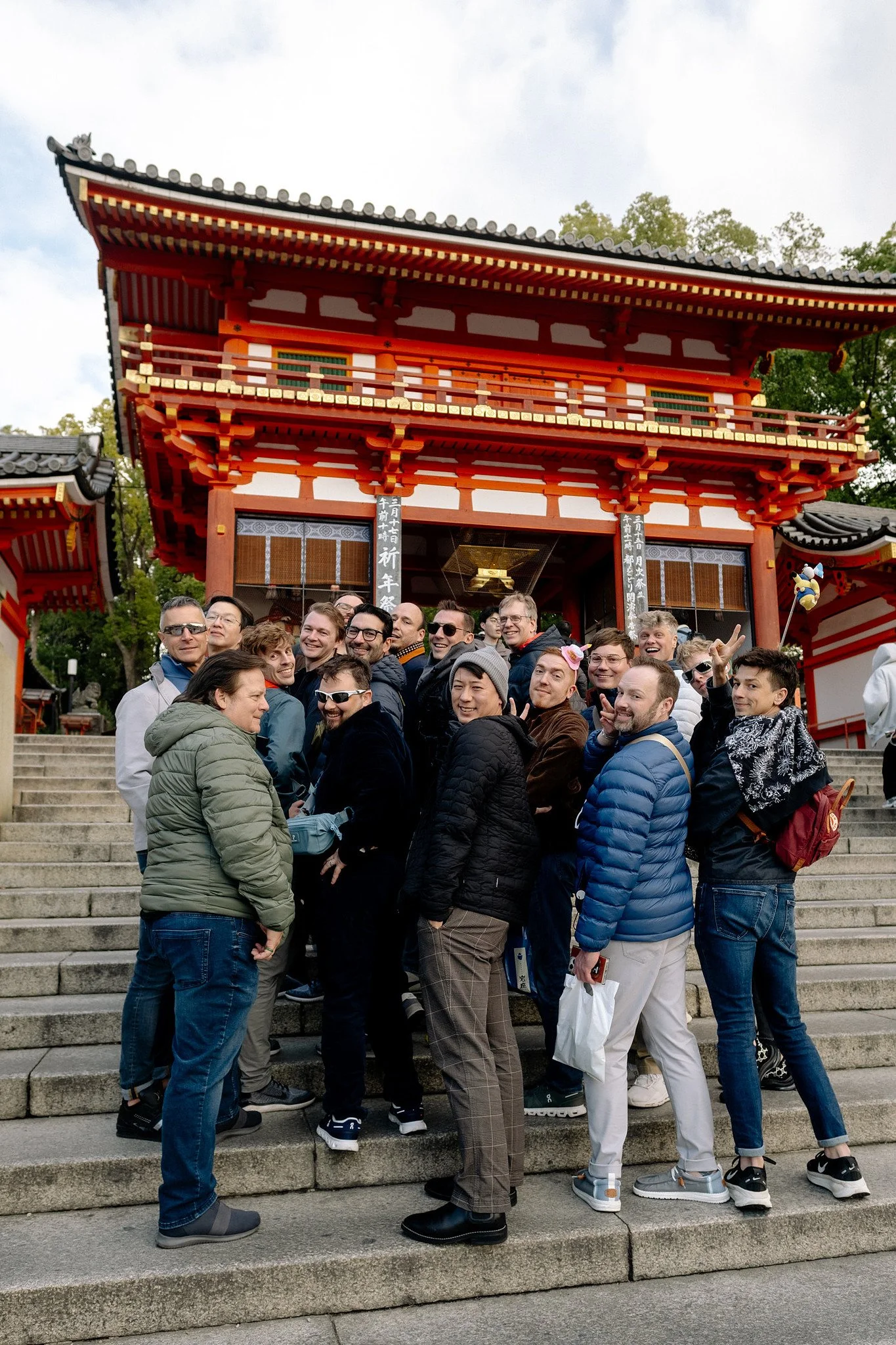  A gay group trip poses on the stone steps of a red and gold temple gate in Kyoto 