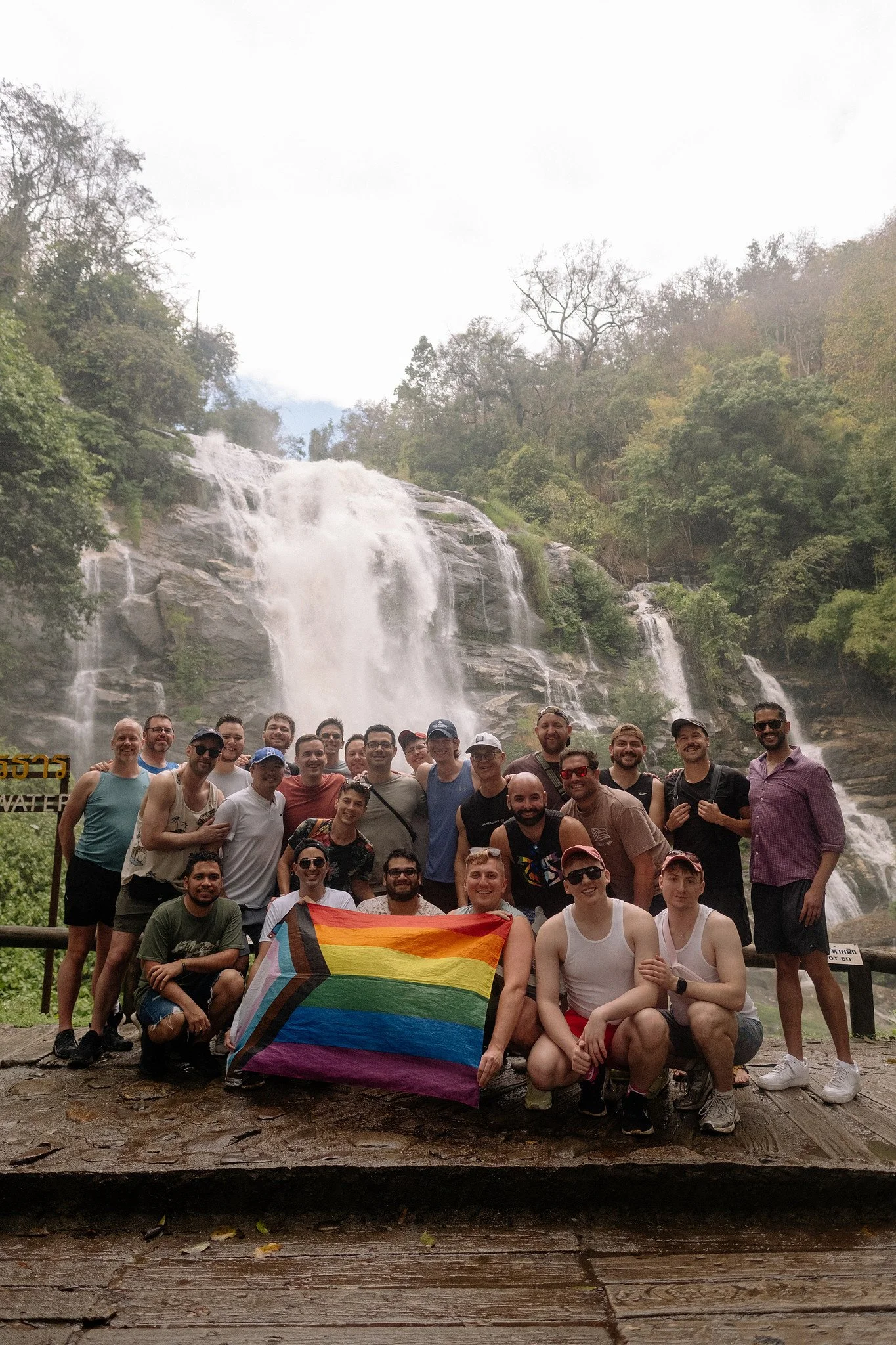  Sidequests LGBTQ+ hikers celebrate with a Pride flag in front of a roaring waterfall outside Chiang Mai 