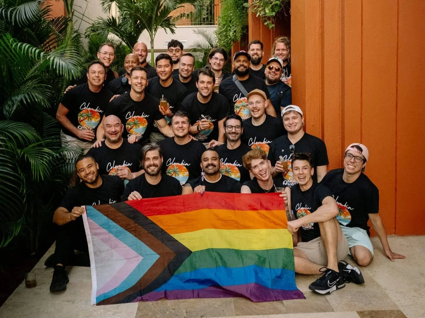 LGBTQ+ travel group holding a Progress Pride flag inside a lush hotel atrium in Colombia.