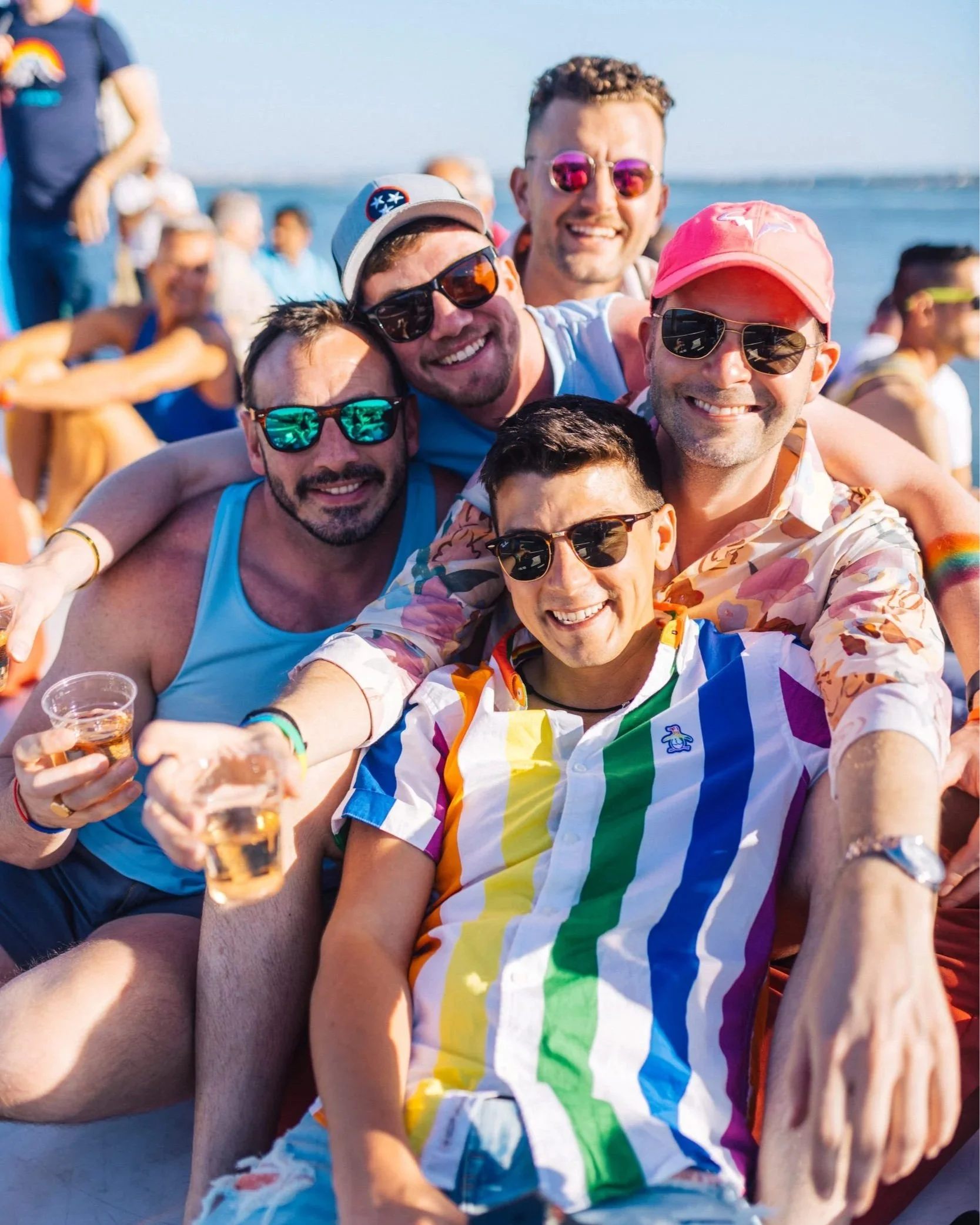 Group of friends in rainbow and pride outfits celebrating on a sunny boat party in Lisbon, Portugal.