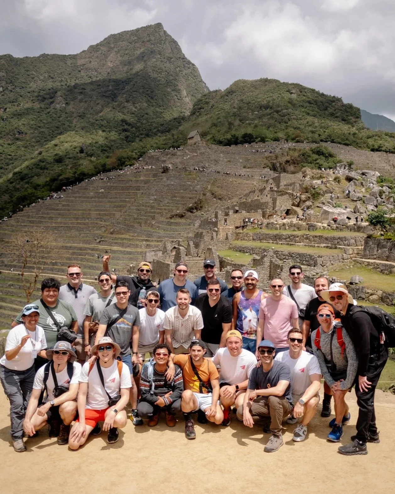 LGBTQ+ travel group posing at Machu Picchu with Inca terraces and Huayna Picchu mountain behind them.