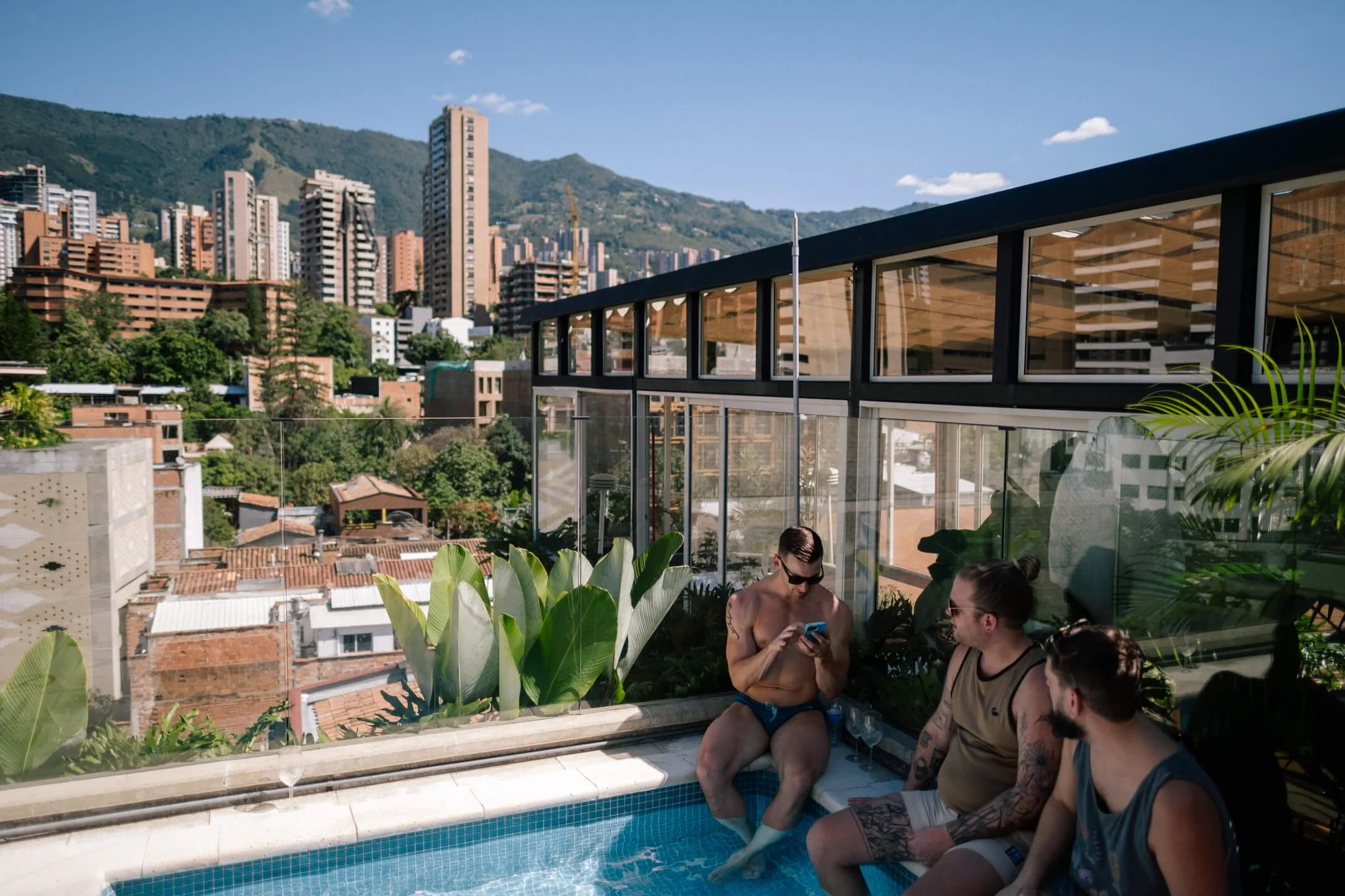 Three men relaxing at a rooftop pool overlooking the El Poblado skyline in Medellín, Colombia.