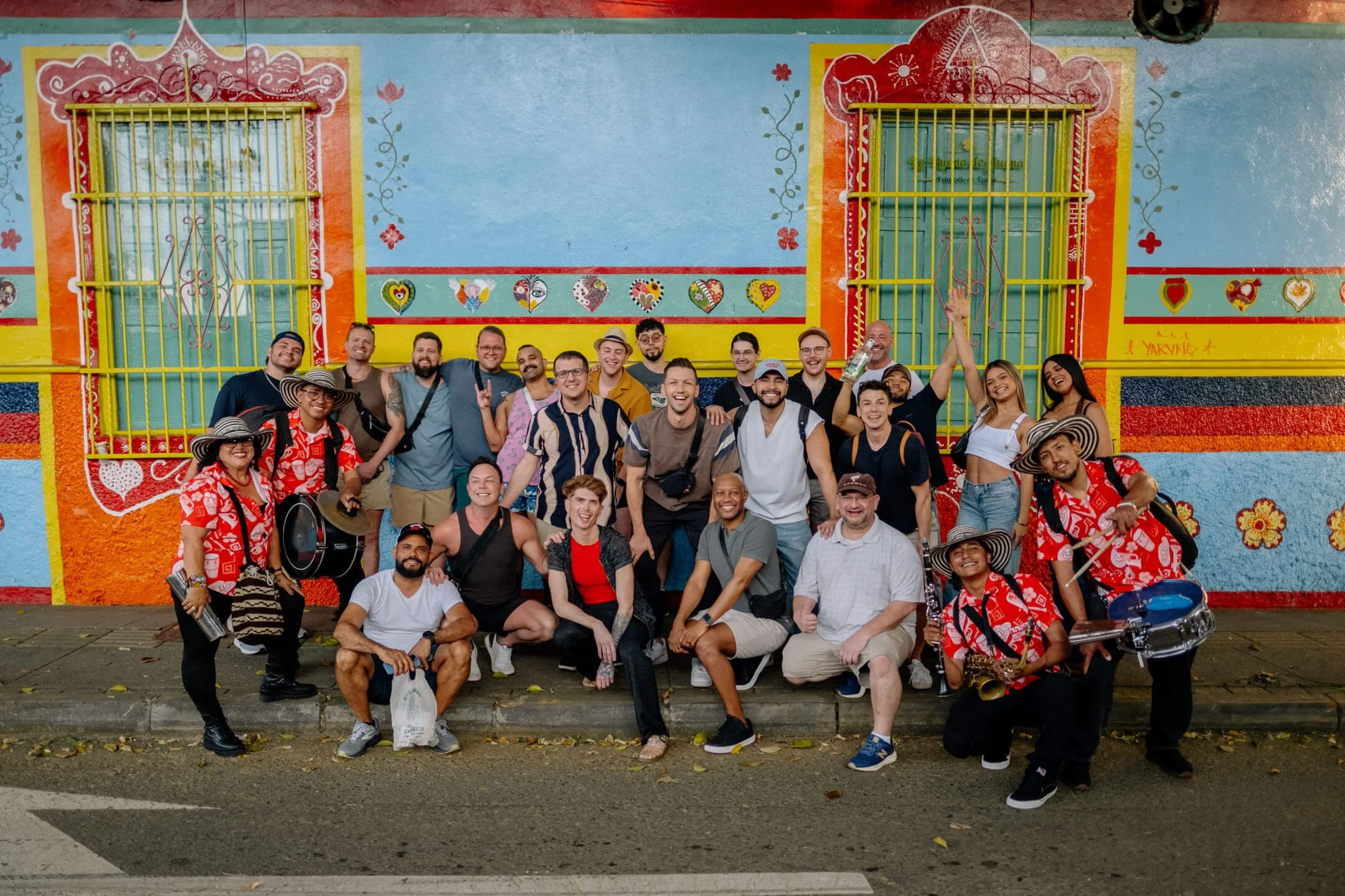 LGBTQ+ travel group posing with a live band in front of a vibrant painted wall in Medellín, Colombia.