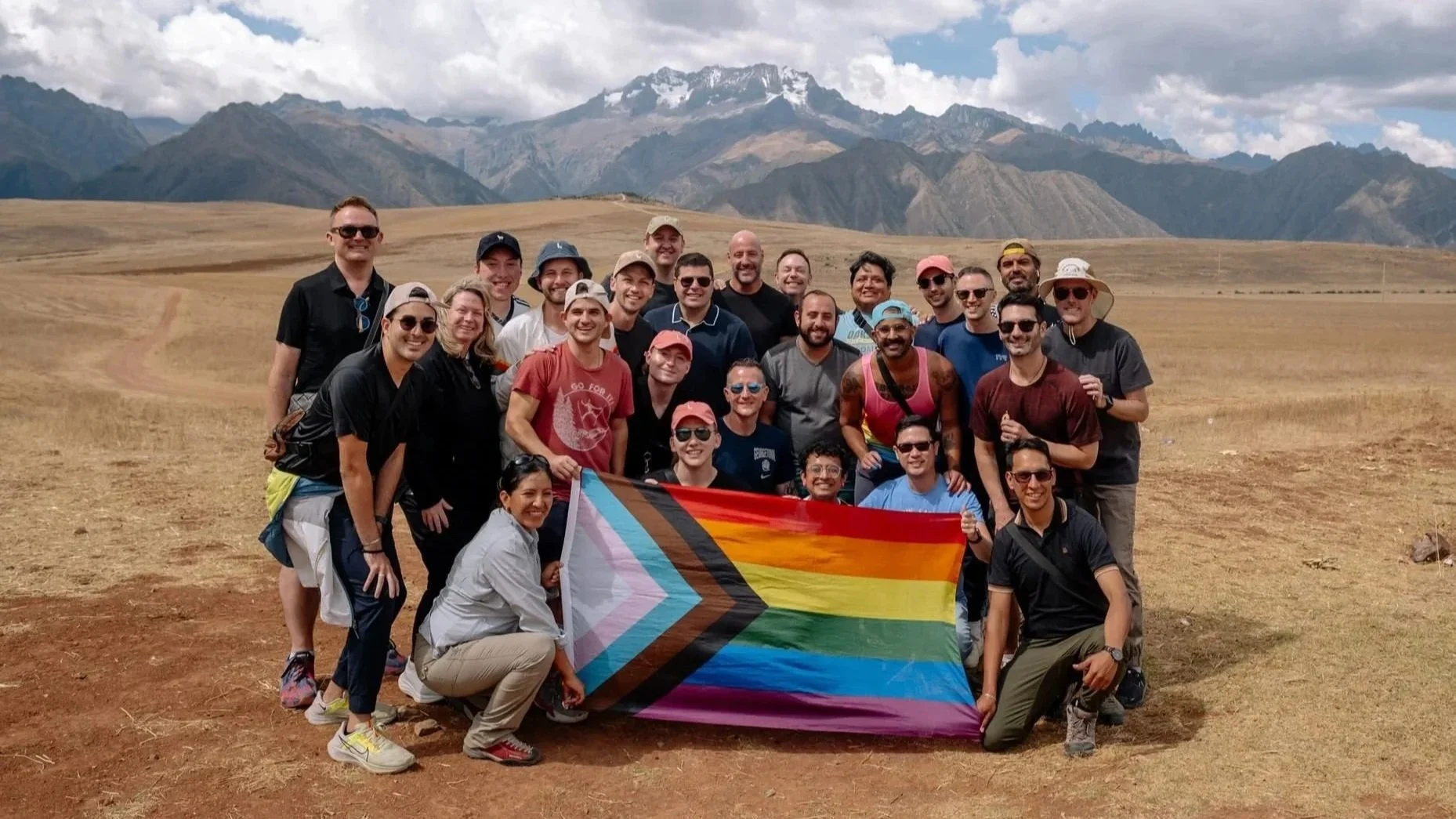 a group of people stand in front of mountains holding a pride flag smiling together