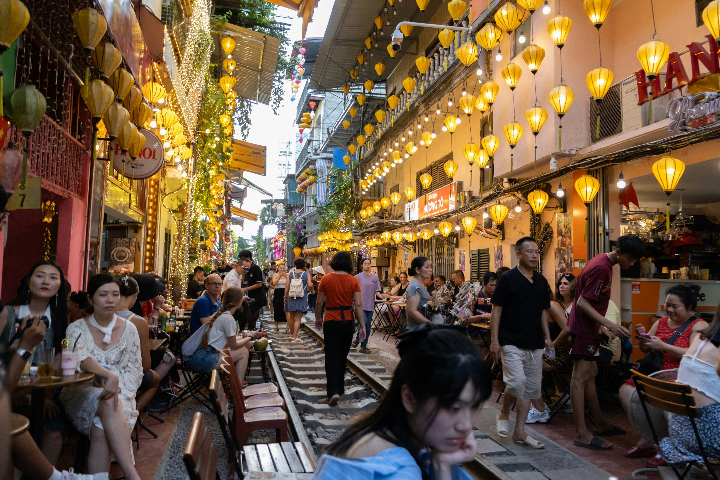 Crowded Hanoi Train Street lined with yellow lanterns and cafes.