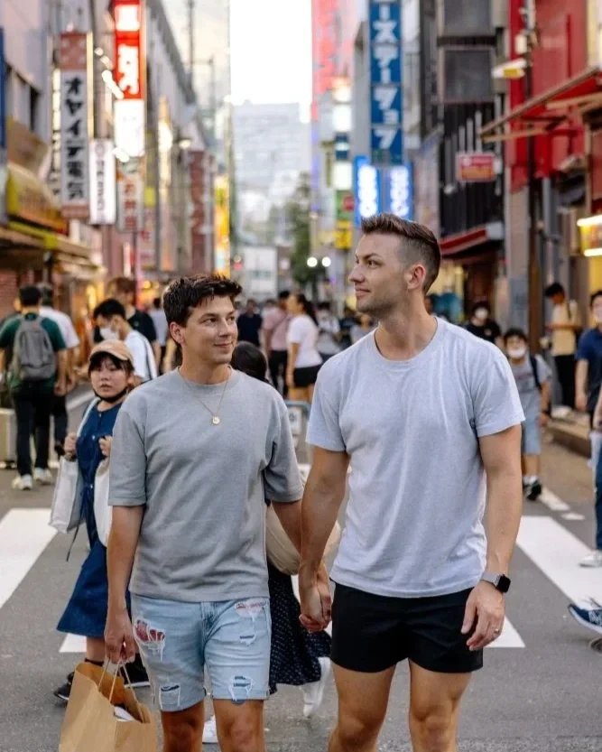 gay couple holding hands walking down a busy street with a shopping bag in Akihabara Tokyo Japan