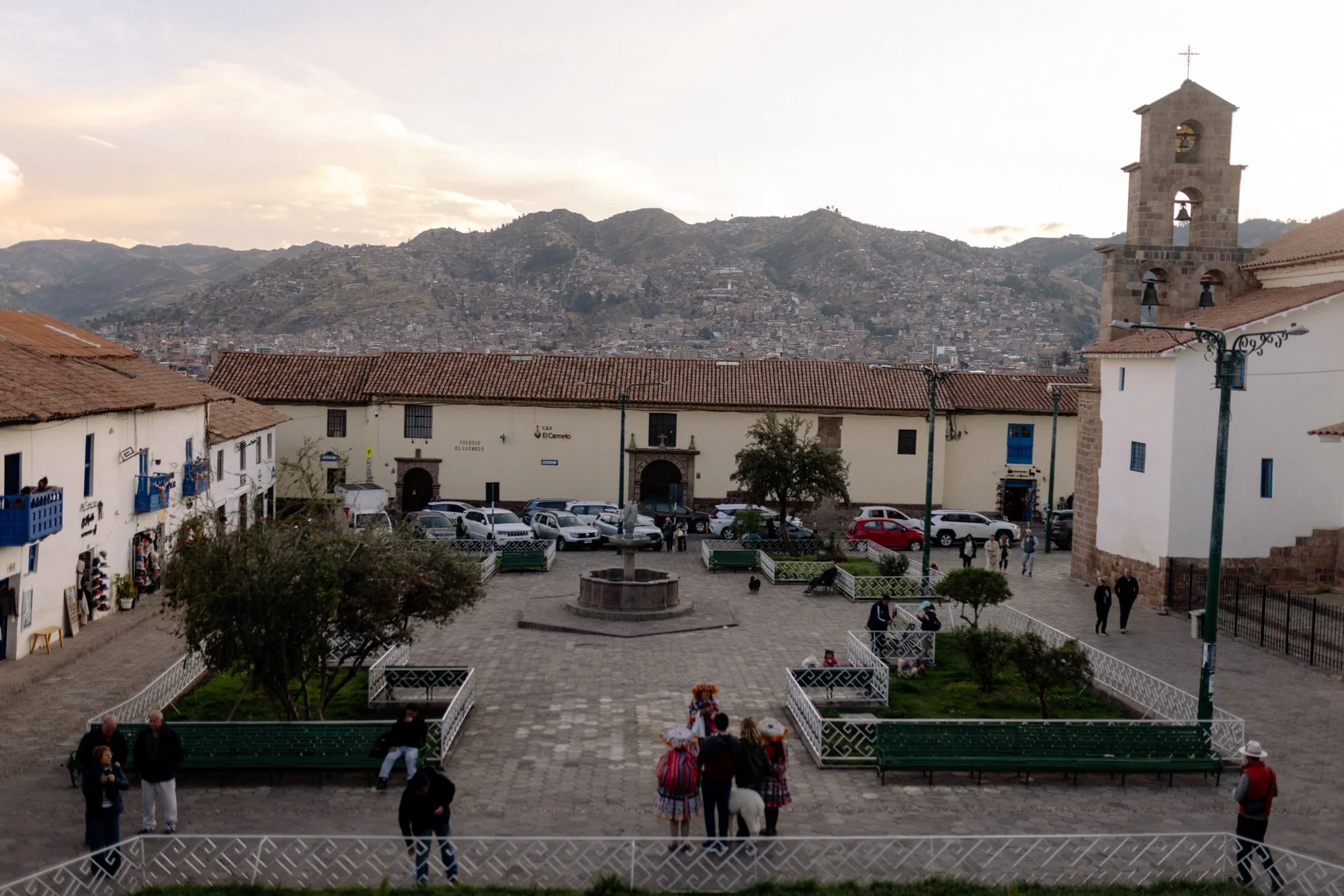 Plaza San Blas in Cusco, Peru, with a stone church bell tower and Andean hillside city views at dusk.