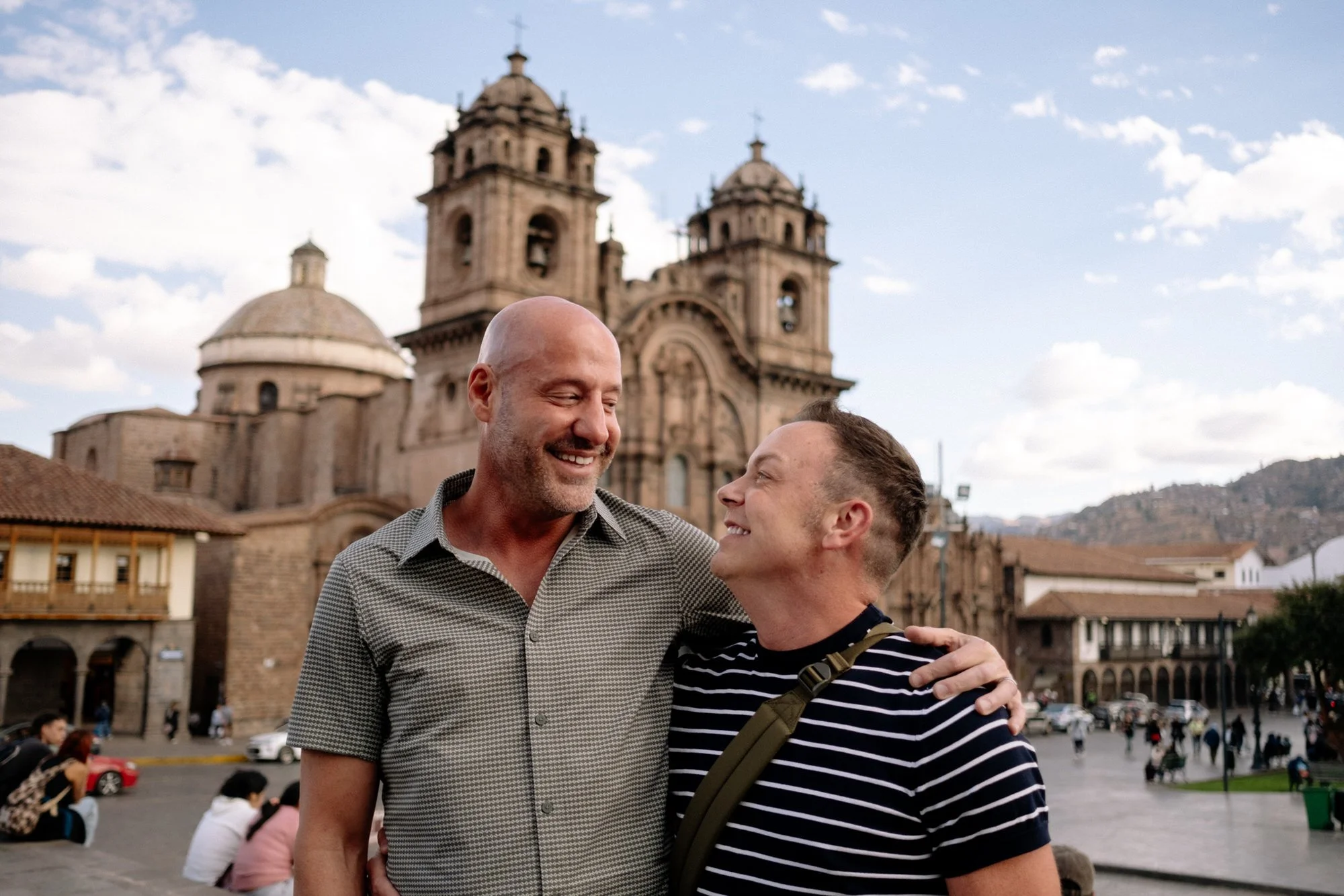 Two men smiling with arms around each other in Plaza de Armas, Cusco, Peru, with the cathedral behind.