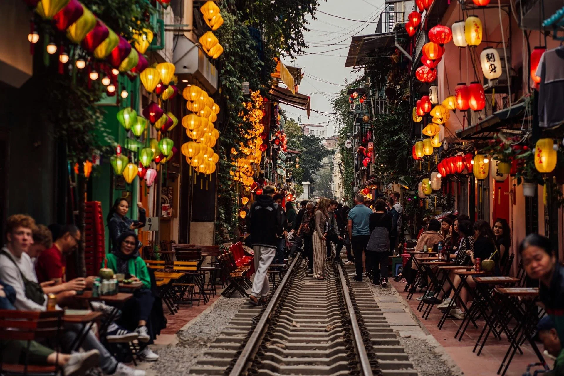Colourful silk lanterns lining a narrow café-lined train track alley in Hanoi's Old Quarter, Vietnam.