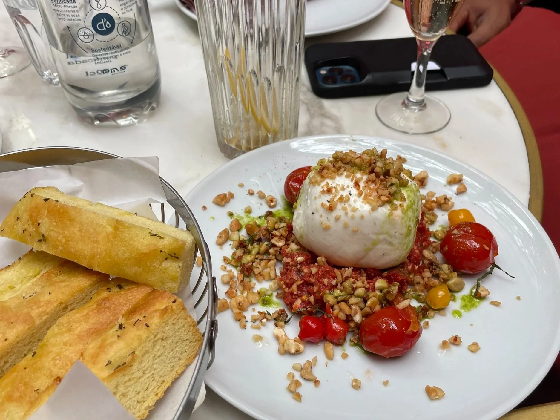 a mozzarella ball with tomatoes and nuts sits on a plate next to a bread basket