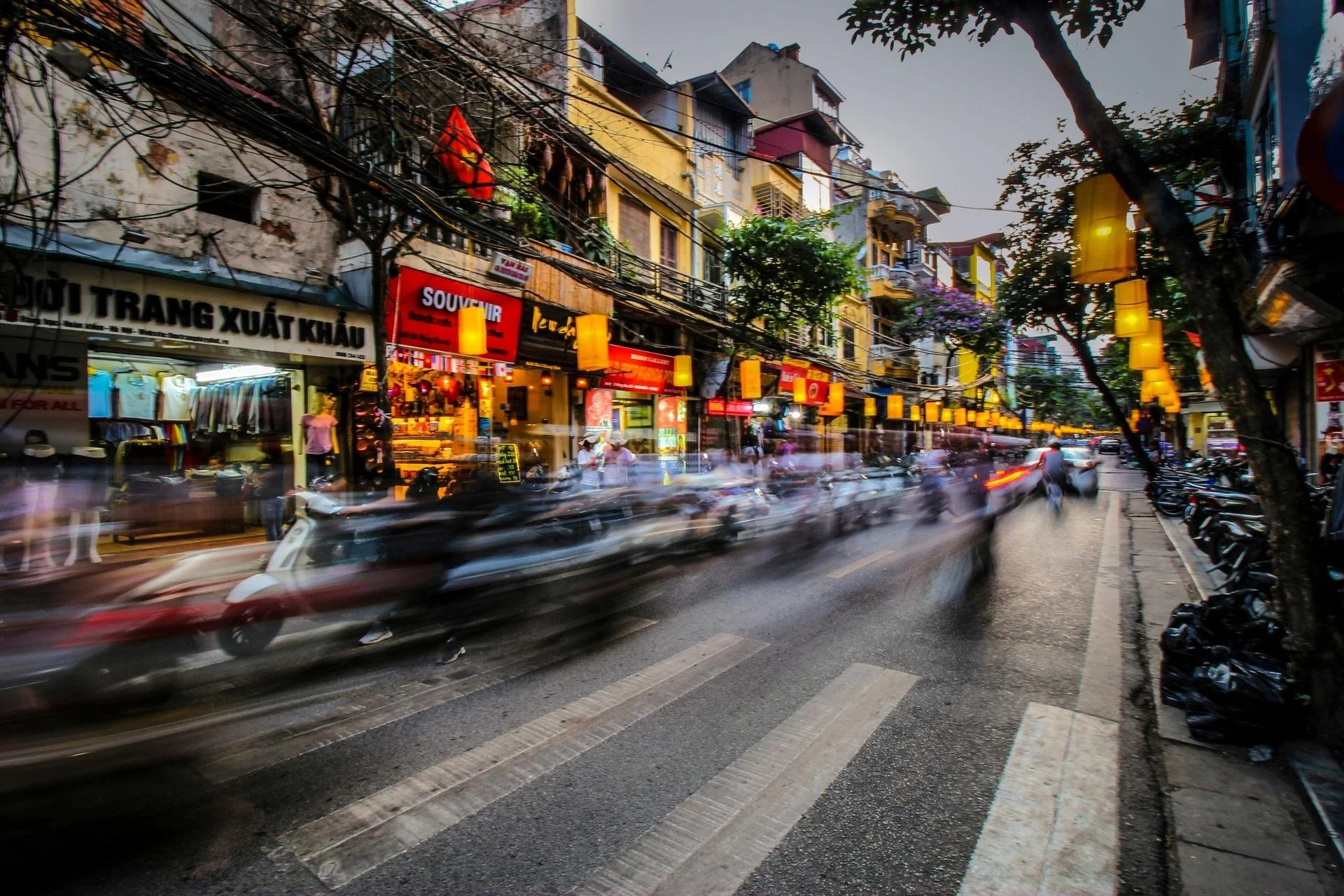 Motorbikes blur past lantern-lit shop fronts on a busy street in Hanoi's Old Quarter, Vietnam.