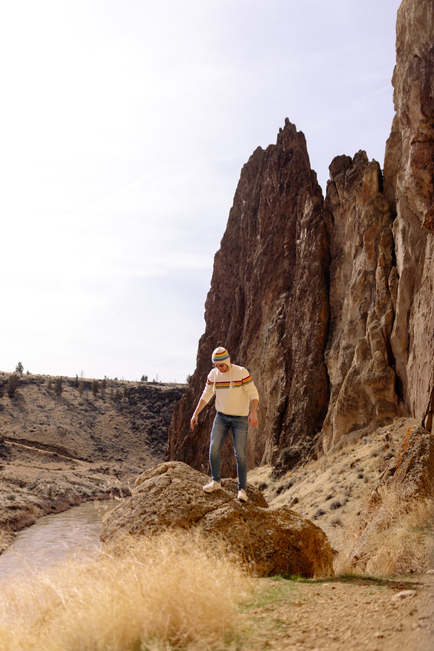Hiker in striped sweater and beanie standing on boulder below Smith Rock spires in Bend, Oregon.