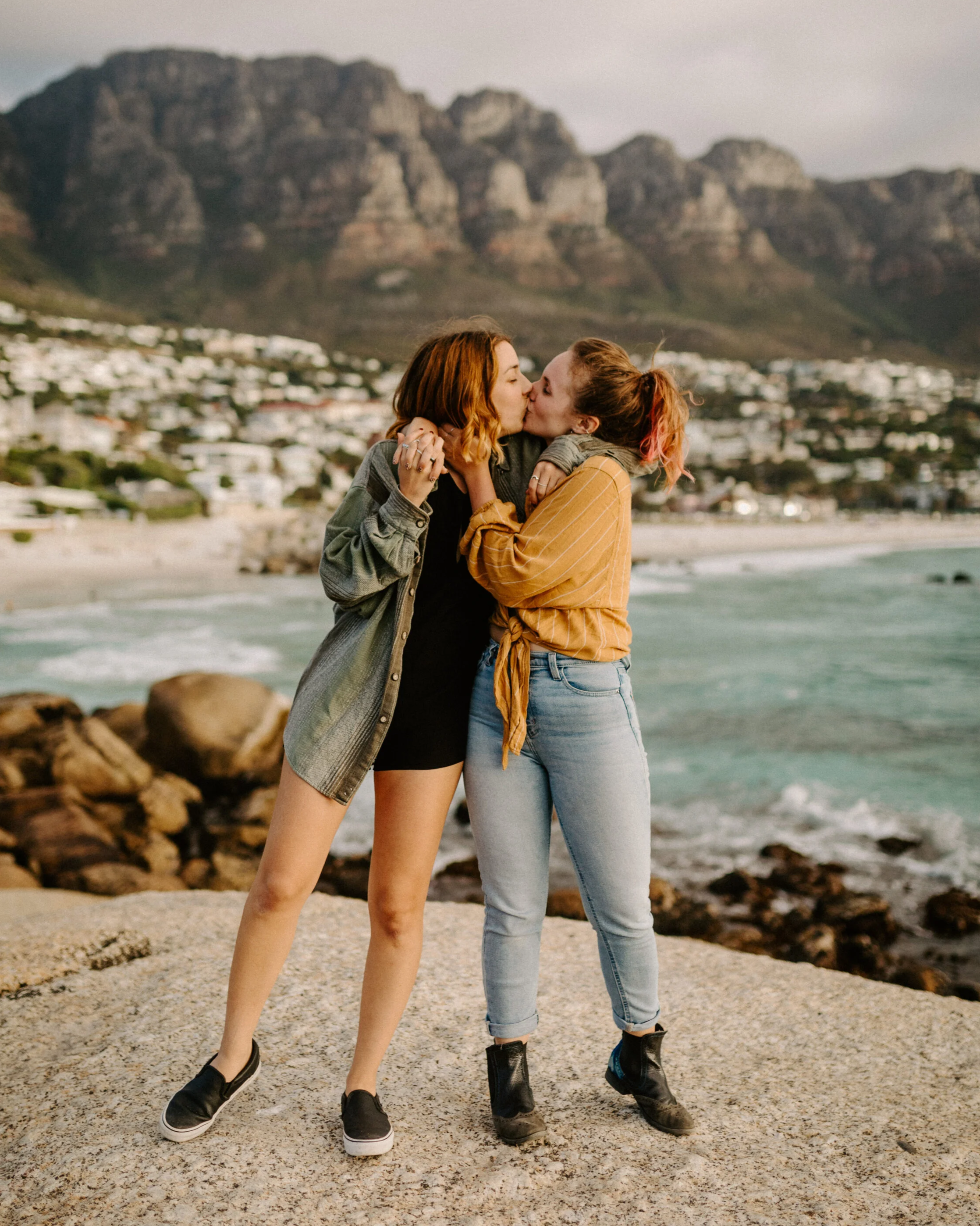 Two women kiss in Cape Town South Africa with a beach and mountains behind them