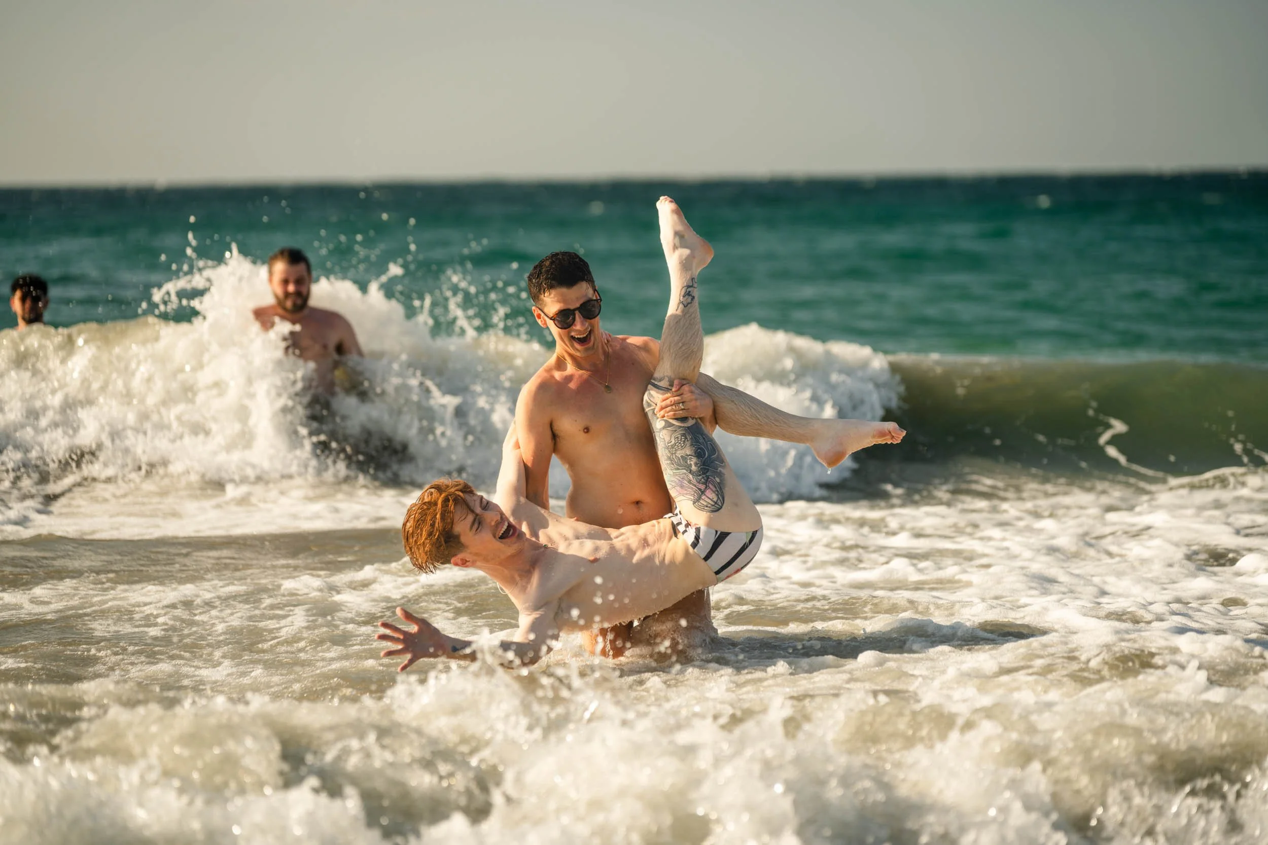 Two men laughing and playing in the ocean surf on a sunny beach in Cartagena, Colombia.