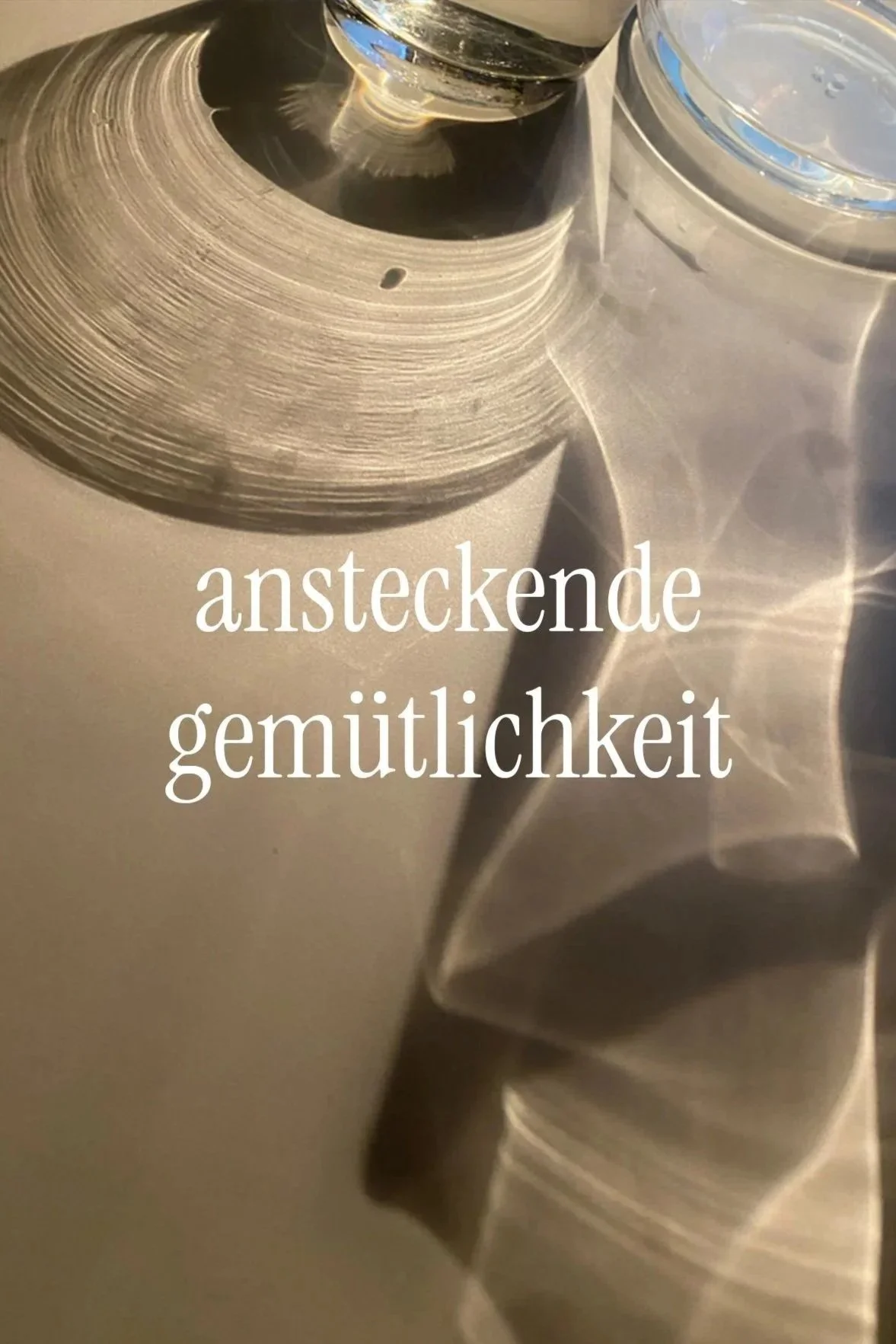 Nahaufnahme eines metallischen, rotierenden Objekts mit Reflexionen und einer Wasserflasche im Hintergrund. Überlagert mit dem deutschen Text 'ansteckende Gemütlichkeit'.
