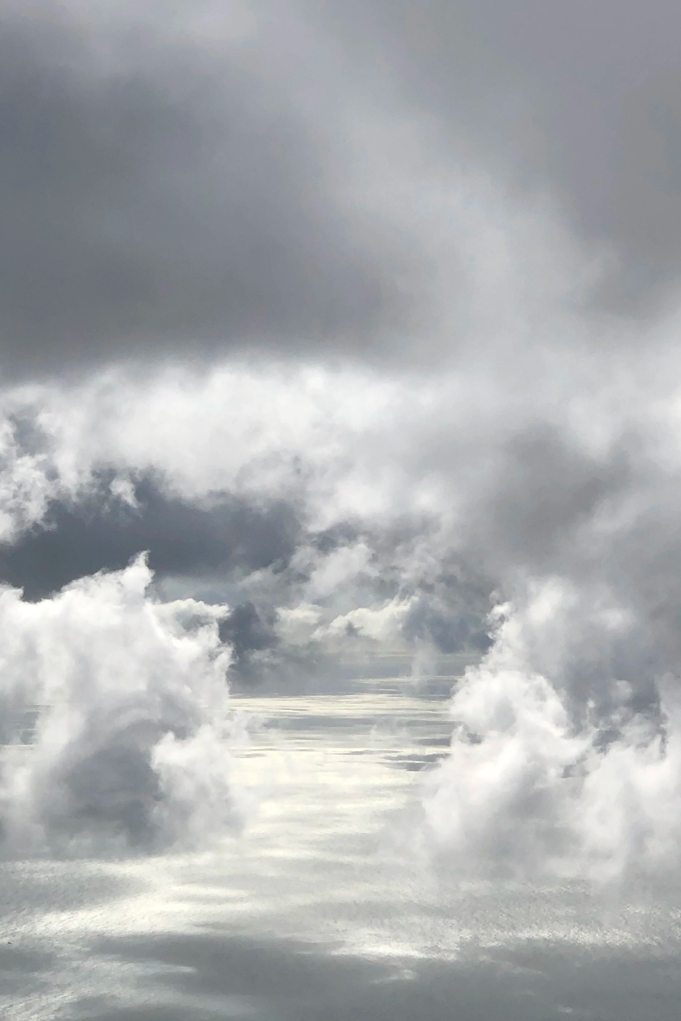 Der Himmel ist wolkenverhangen mit dunklen und hellen Wolken, die sich über einem ruhigen See spiegeln.