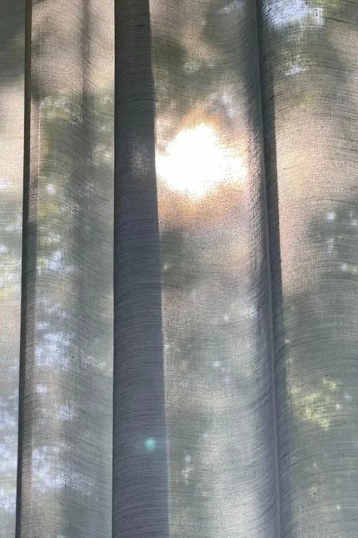 Sonnenlicht scheint durch eine halbtransparente Gardine, wodurch Lichtflecken und Schatten sichtbar werden.