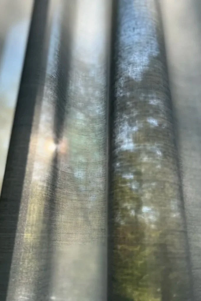 Blick durch eine schimmernde, metallische Oberfläche mit reflektierenden vertikalen Linien, die an einen Stoff oder eine Metallstruktur erinnern.