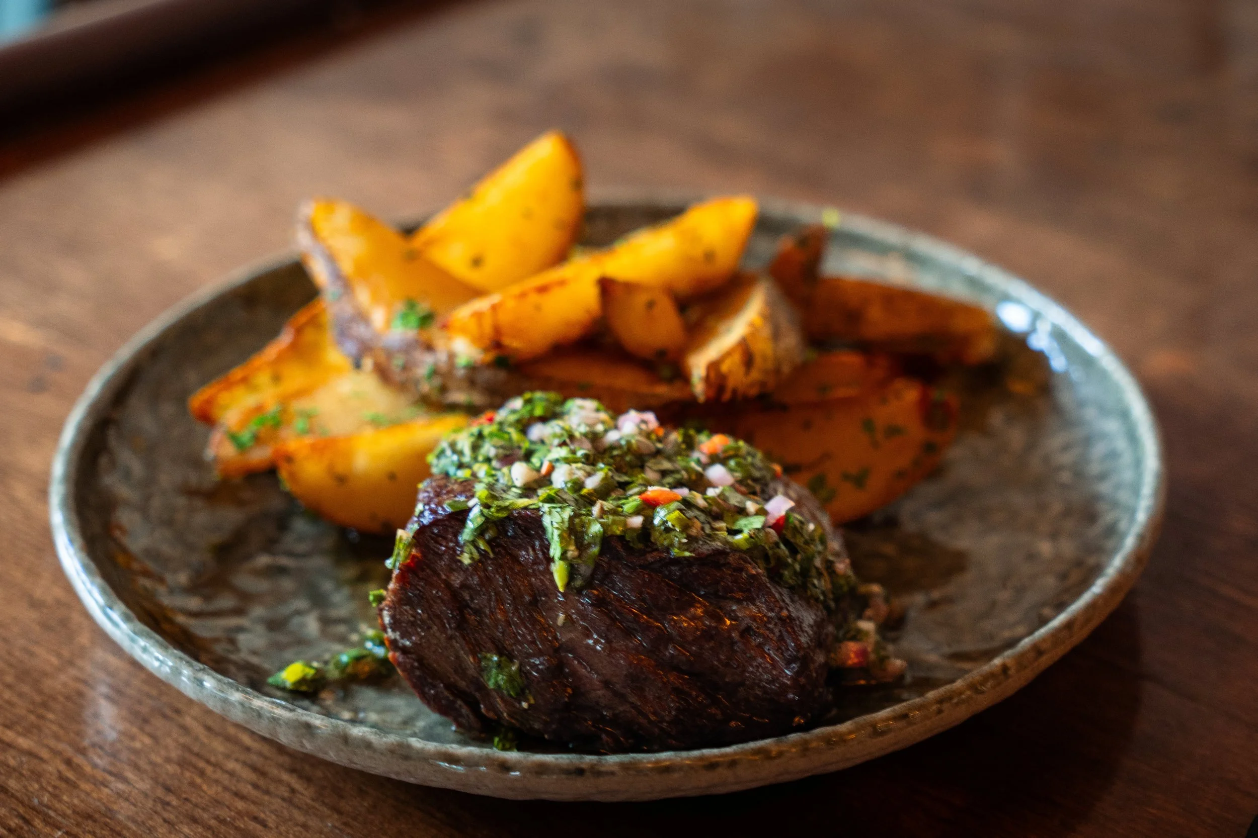 Prime bavette steak at Gunny’s Pub in Lincoln Park, deeply seared and topped with bright salsa verde, served alongside golden wedge-cut potatoes tossed with garlic and herbs. Pub steak, taken very seriously