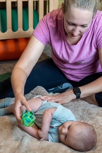 baby rolling to toy with therapist