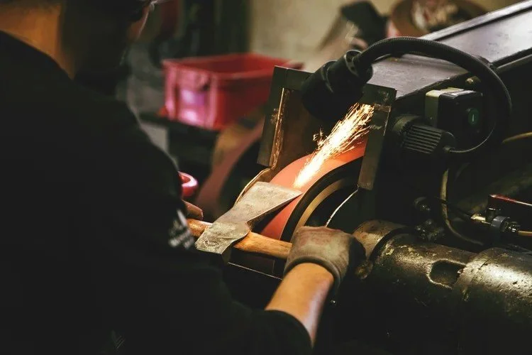 Fabricator grinding a steel part as sparks fly from the machine.