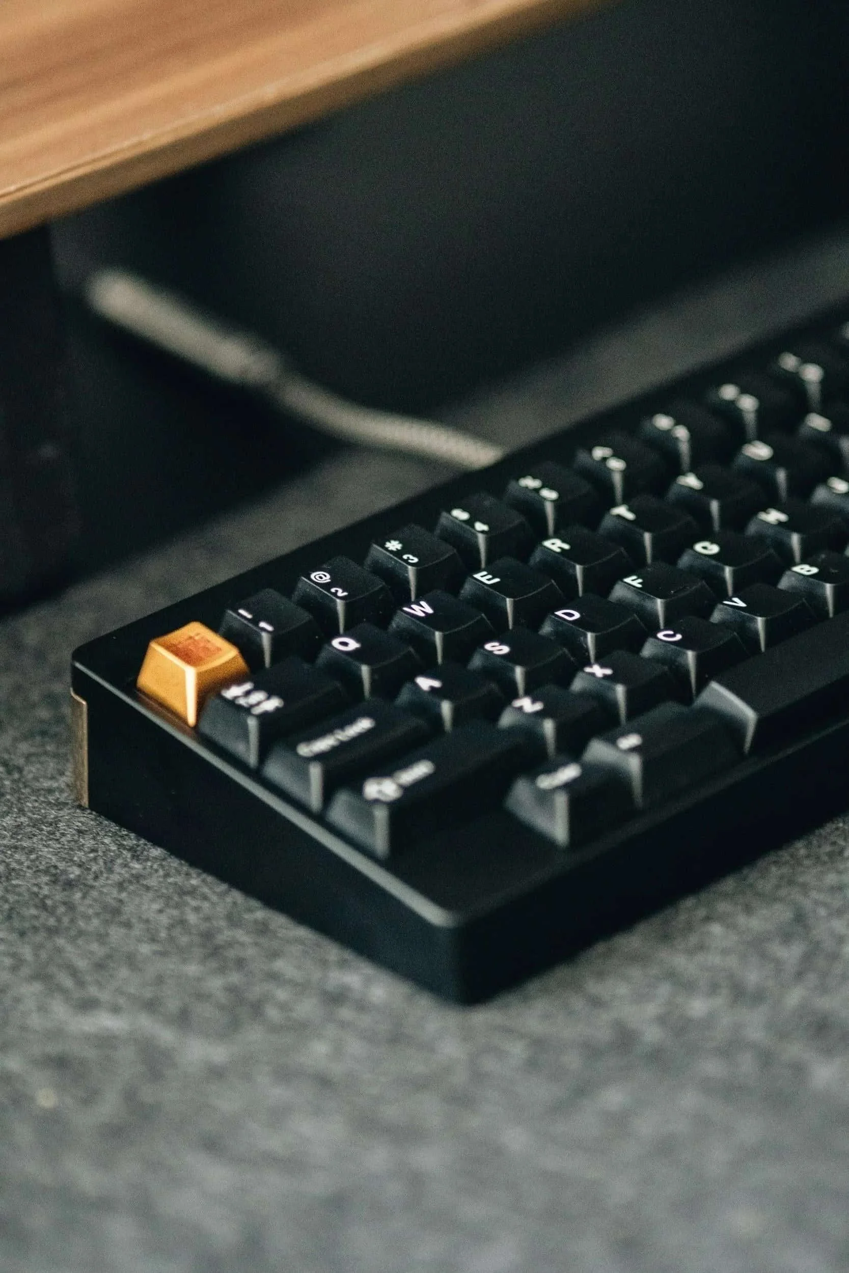 A close up shot of a physical mechanical keyboard that is black with one accent button for the escape key.