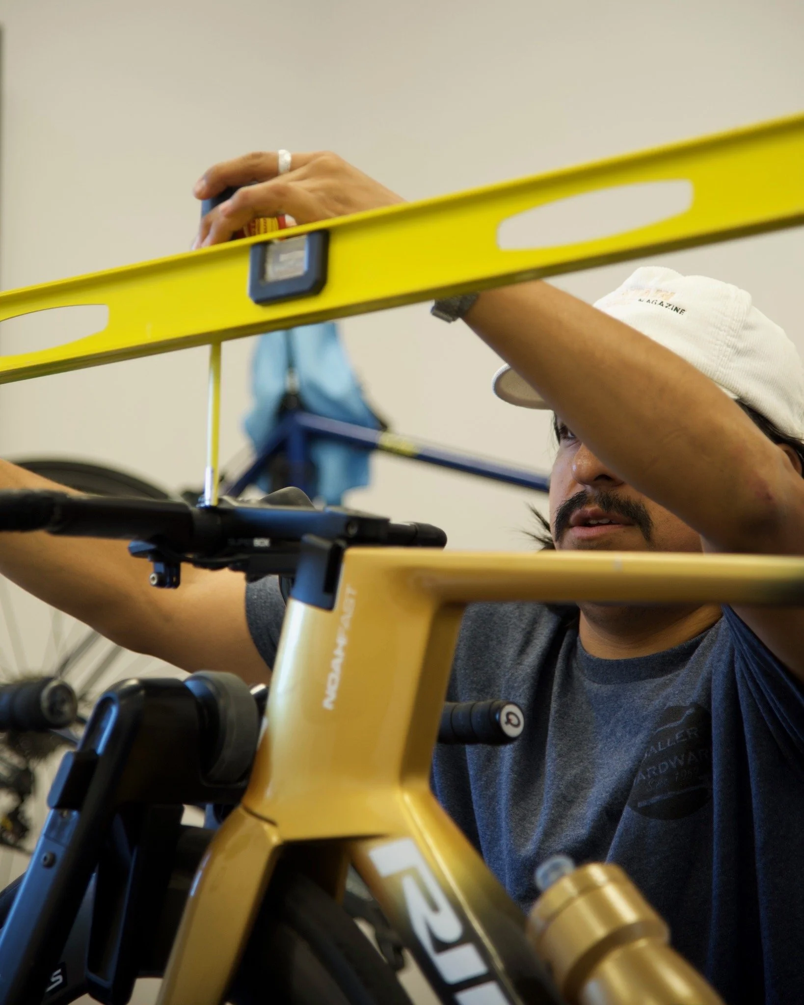 A person adjusting a yellow mountain bike with black and gold components using a level tool on a wall.