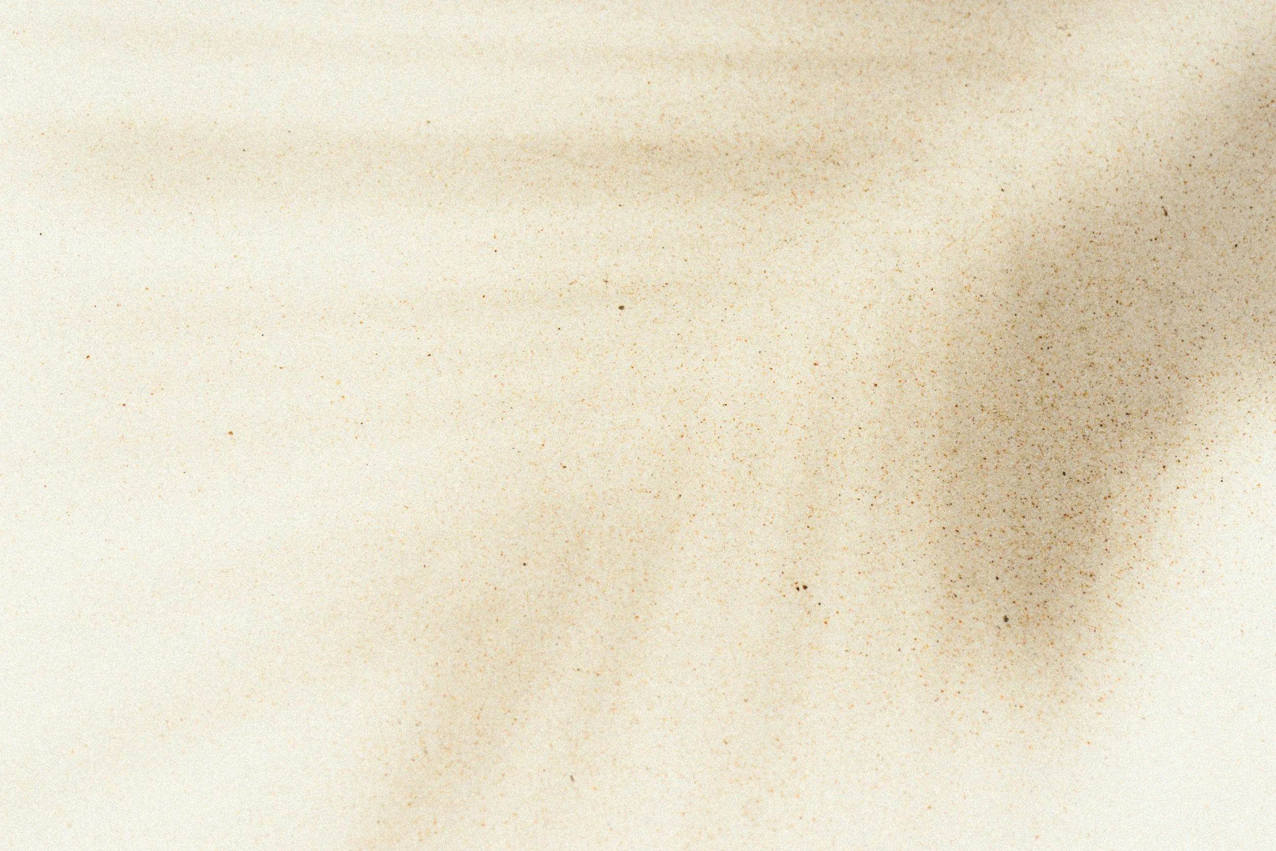 Close-up of a sandy surface with some scattered darker grains and a blurred shadow.