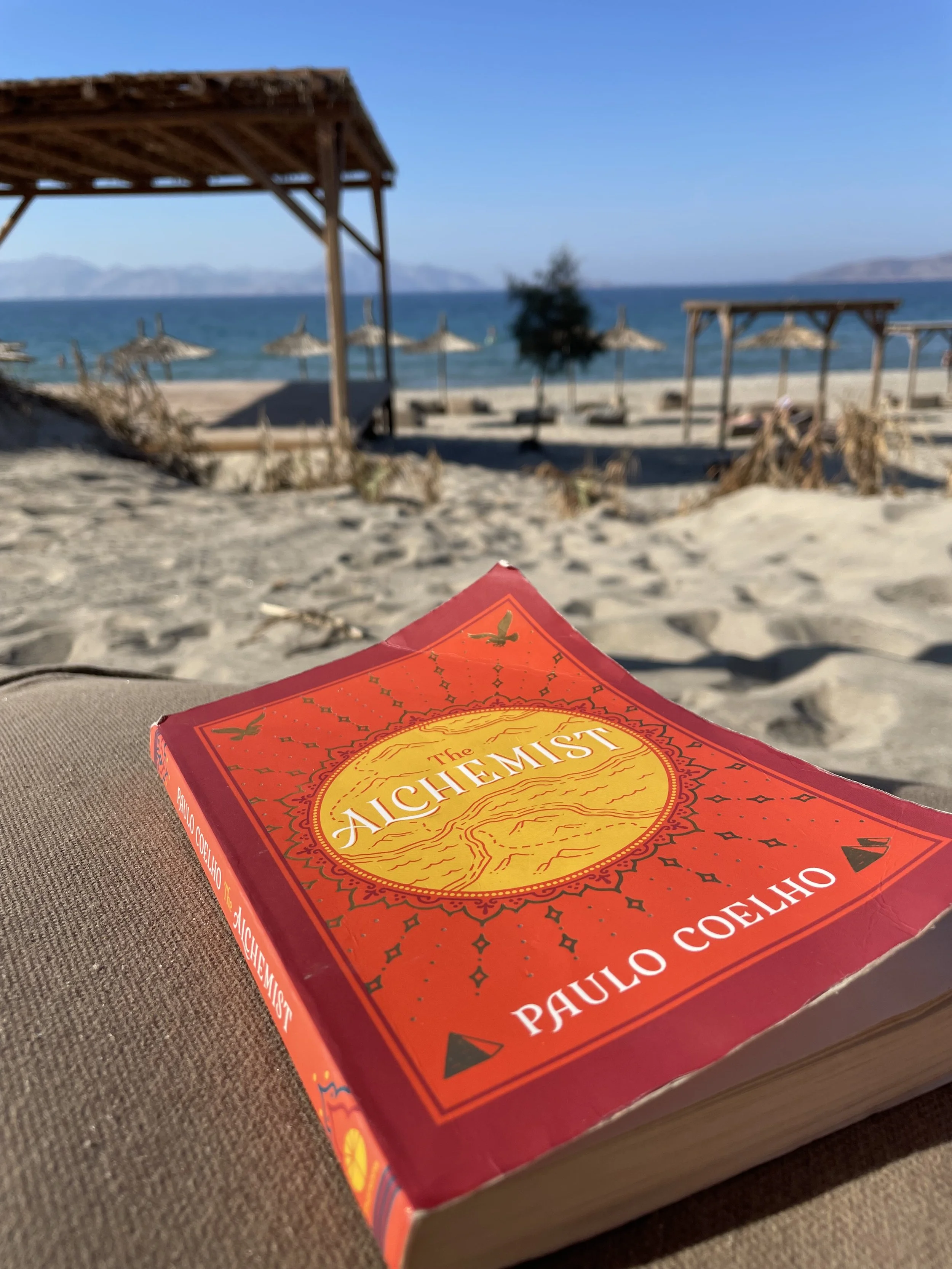 The Alchemist book on a beach — symbolizing clarity, purpose, and soulful business journeys.