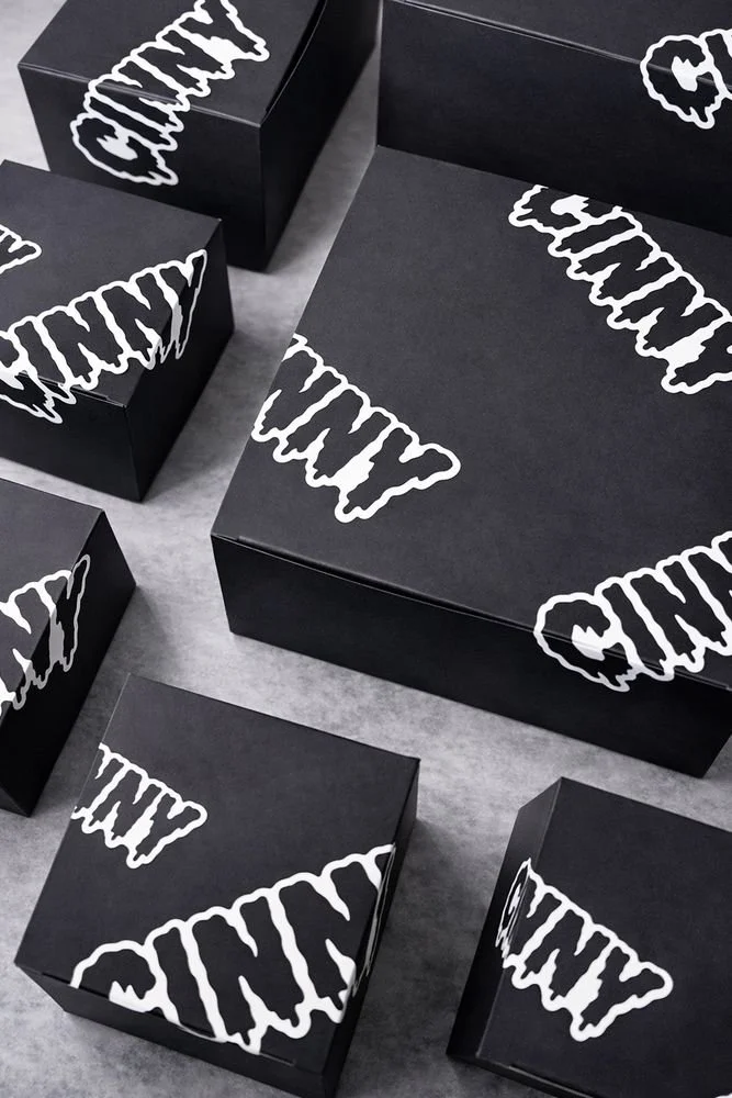 Black boxes with white, dripping-style text that reads 'CINNY' on the lids, positioned on a gray surface.