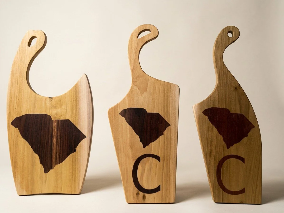 Three wood charcuterie boards with inlaid South Carolina state shapes and letter C designs by Saluda Dog Woodworks