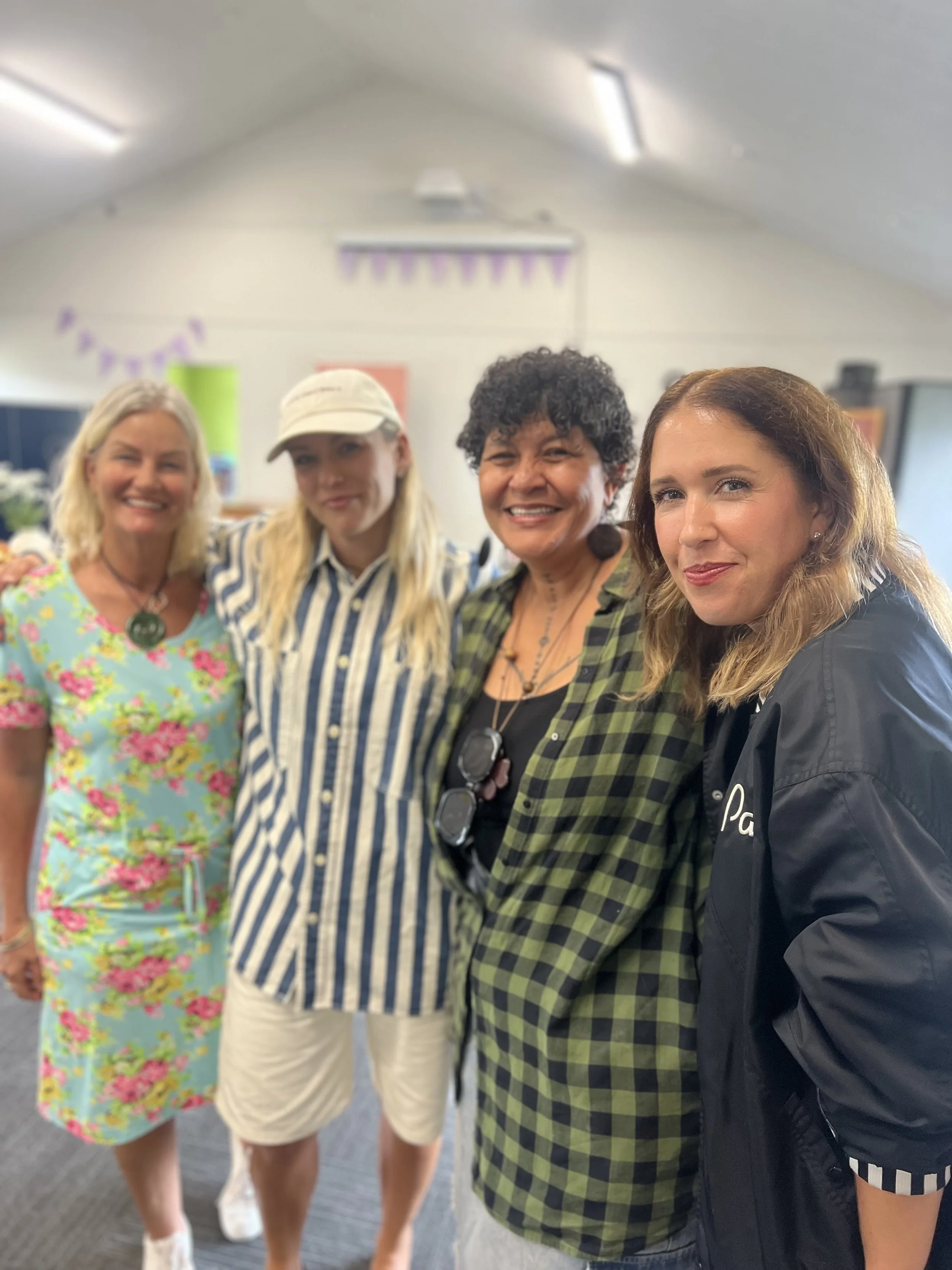 Four women standing close together indoors, smiling at the camera, with a decorated room in the background.