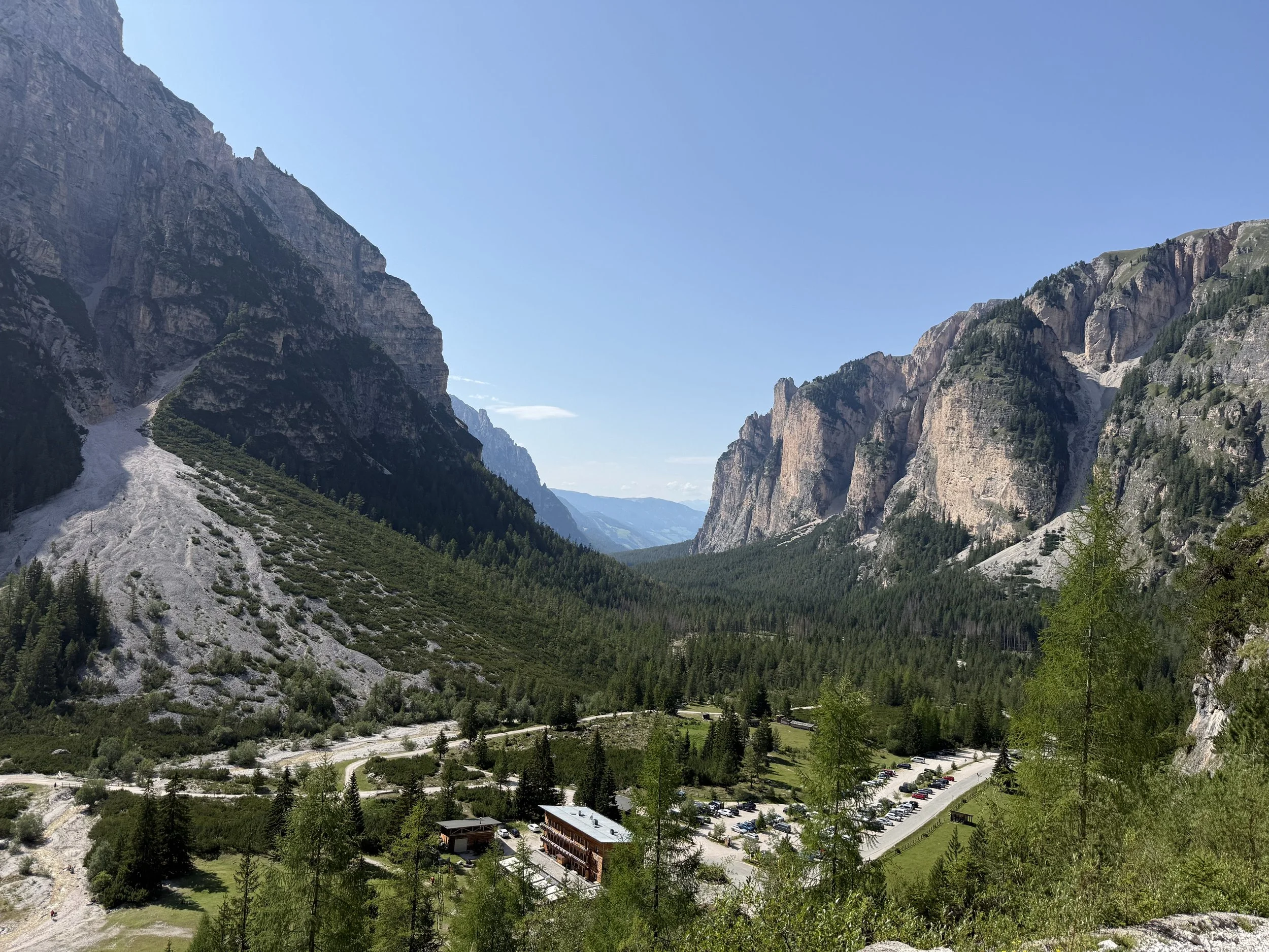 Mountain landscape with rocky cliffs, green forest, and a valley view under a clear blue sky.